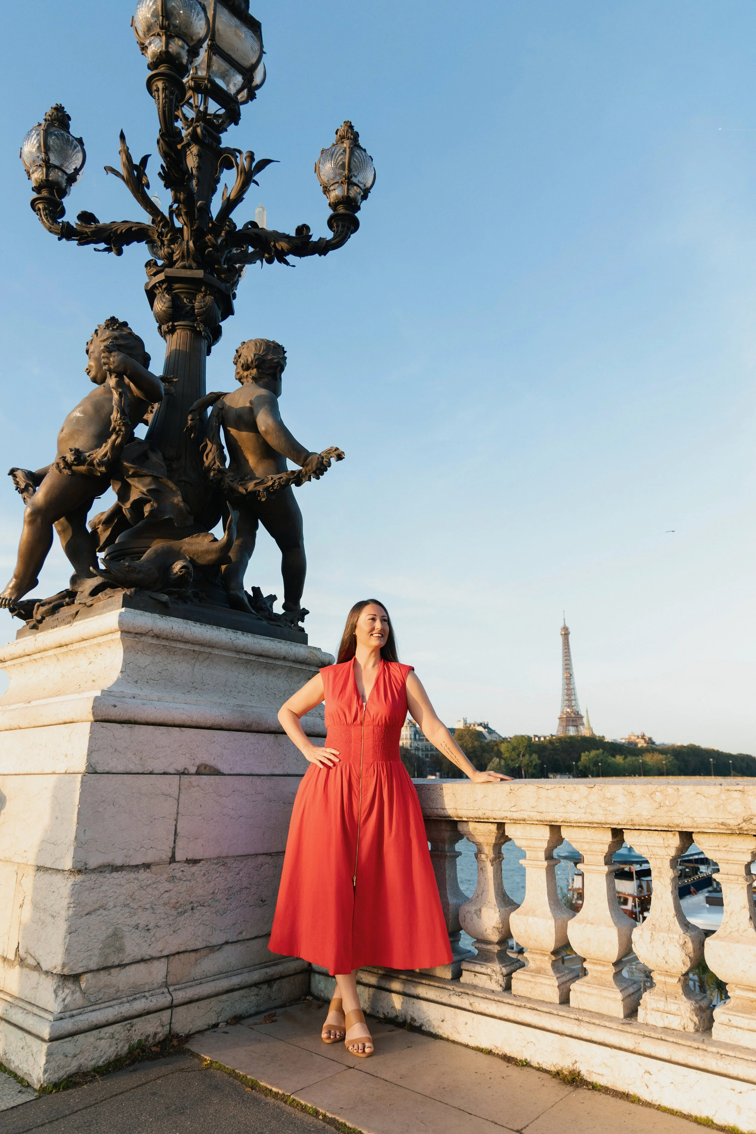 A woman in a red dress standing on a Paris bridge with the Eiffel Tower in the background. Destination Paris portrait photographer