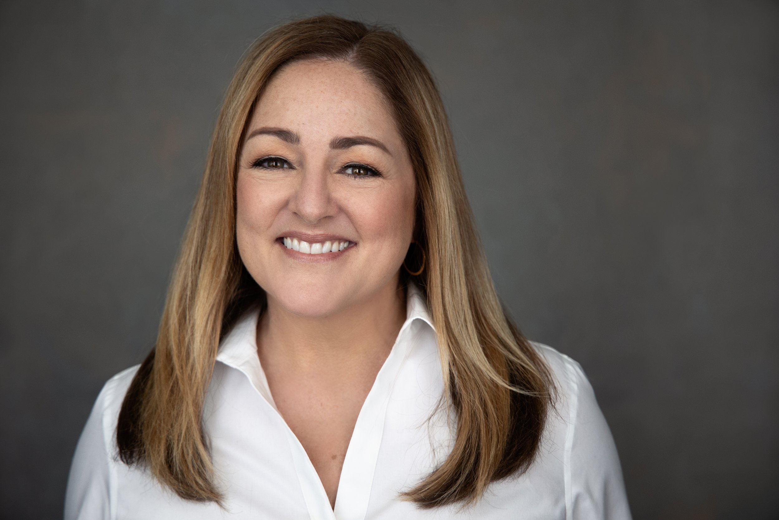 A woman with dark hair lying on her side, resting her head on her hand and smiling at the camera.
