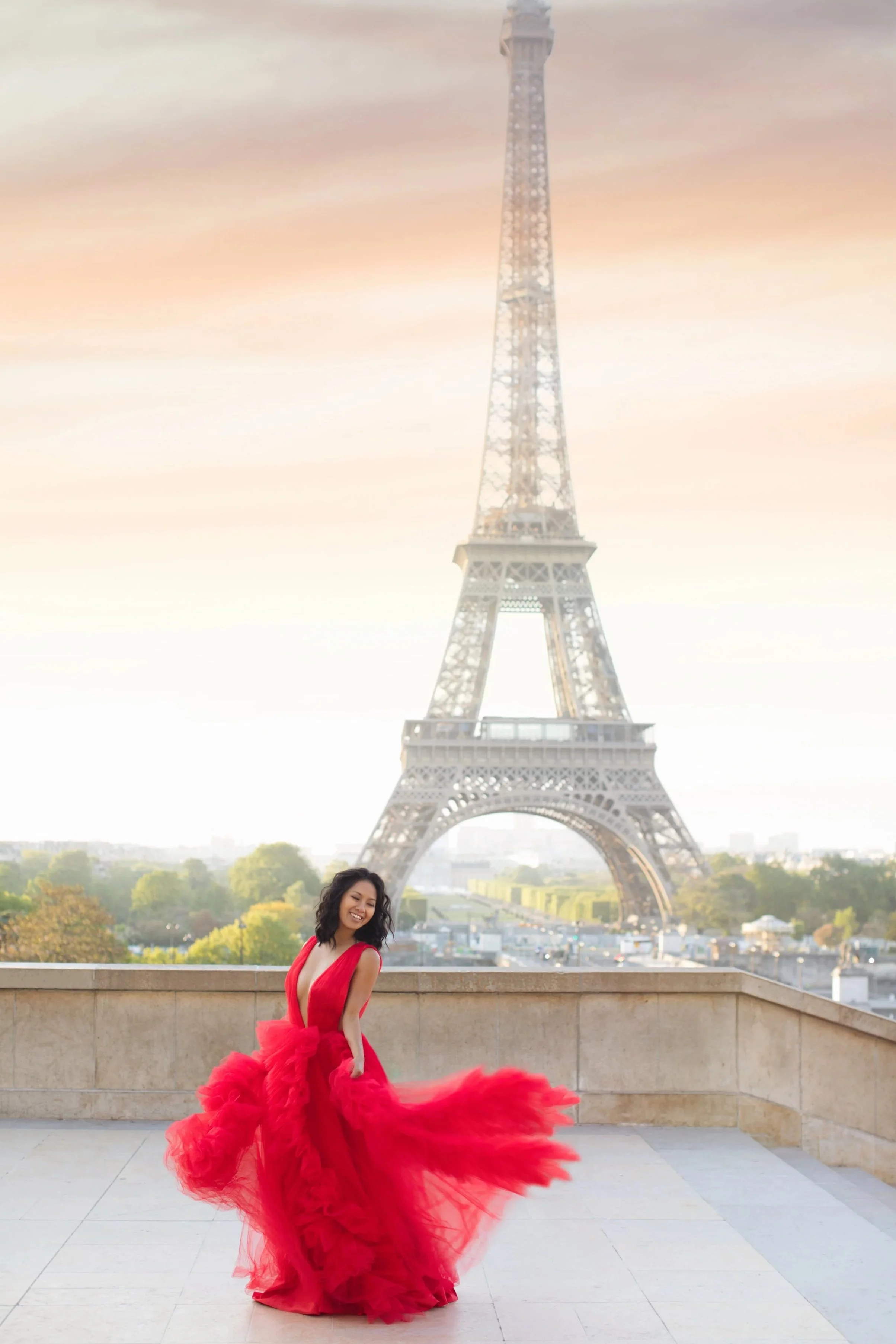A woman in a flowing red dress dancing on a terrace with the Eiffel Tower in the background during sunset.