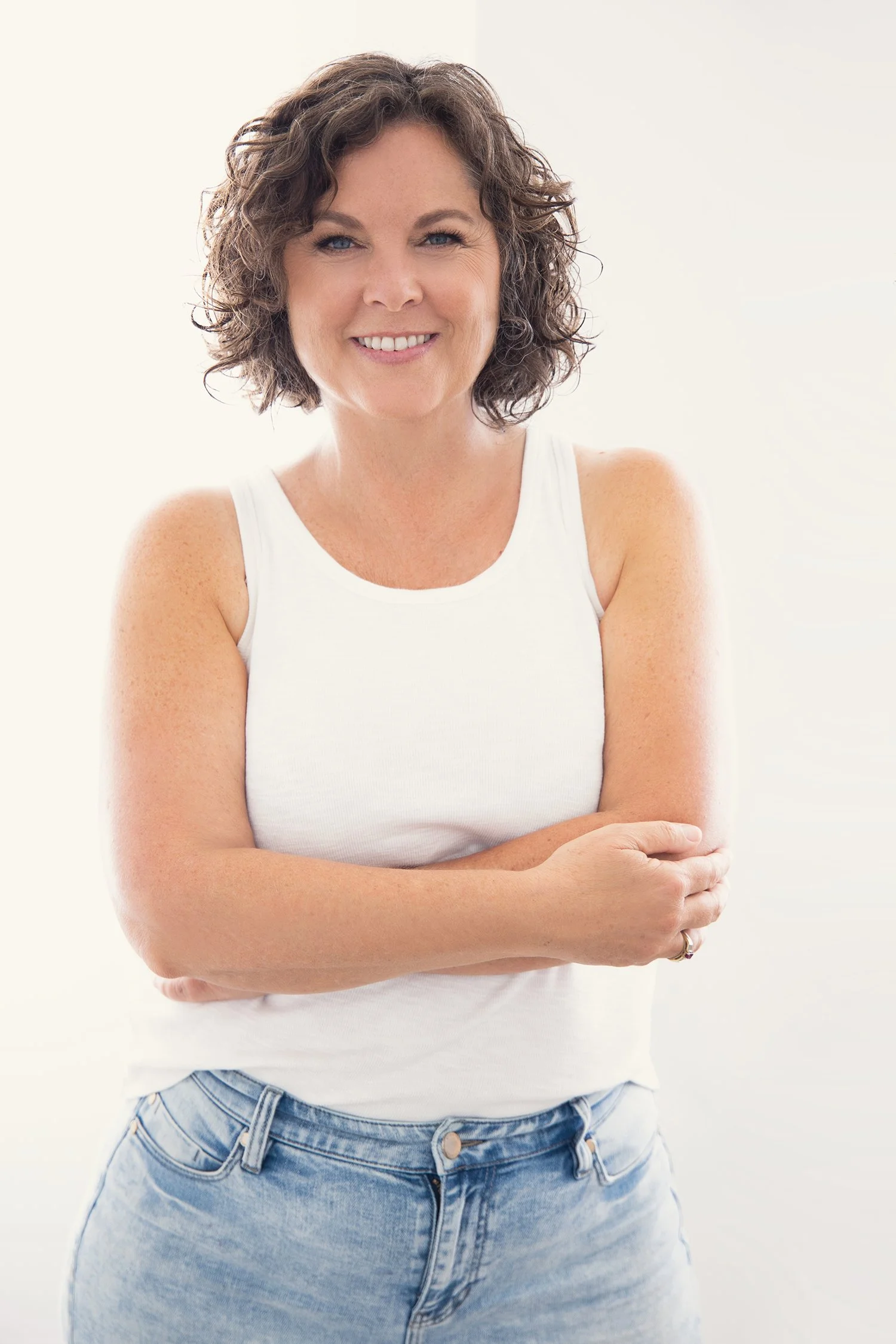 A woman with curly dark hair wearing a sleeveless, sparkly silver dress and large turquoise earrings, smiling at the camera against a dark background.