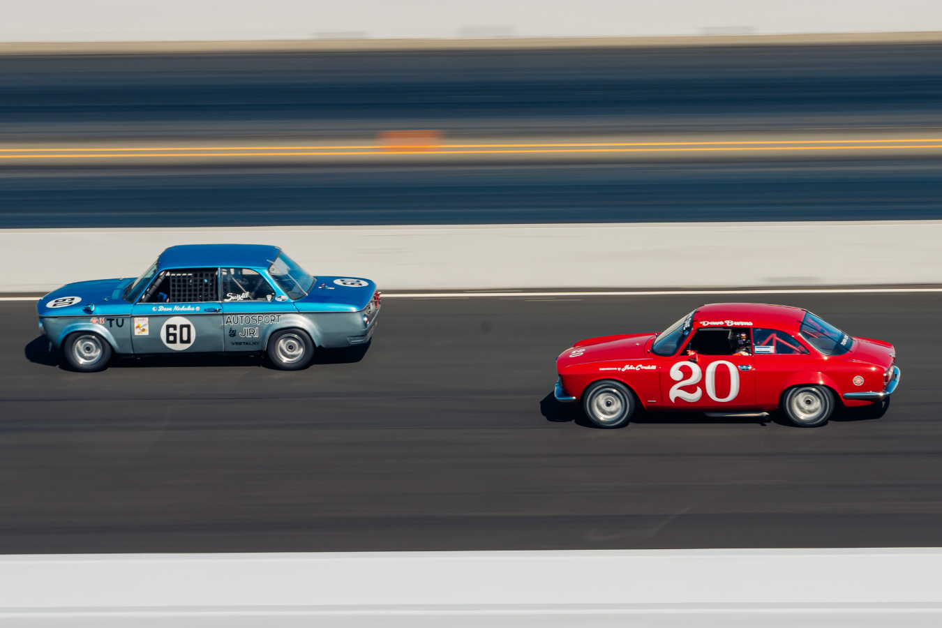 Two vintage race cars, one blue and one red, racing on a track with a blurred background.