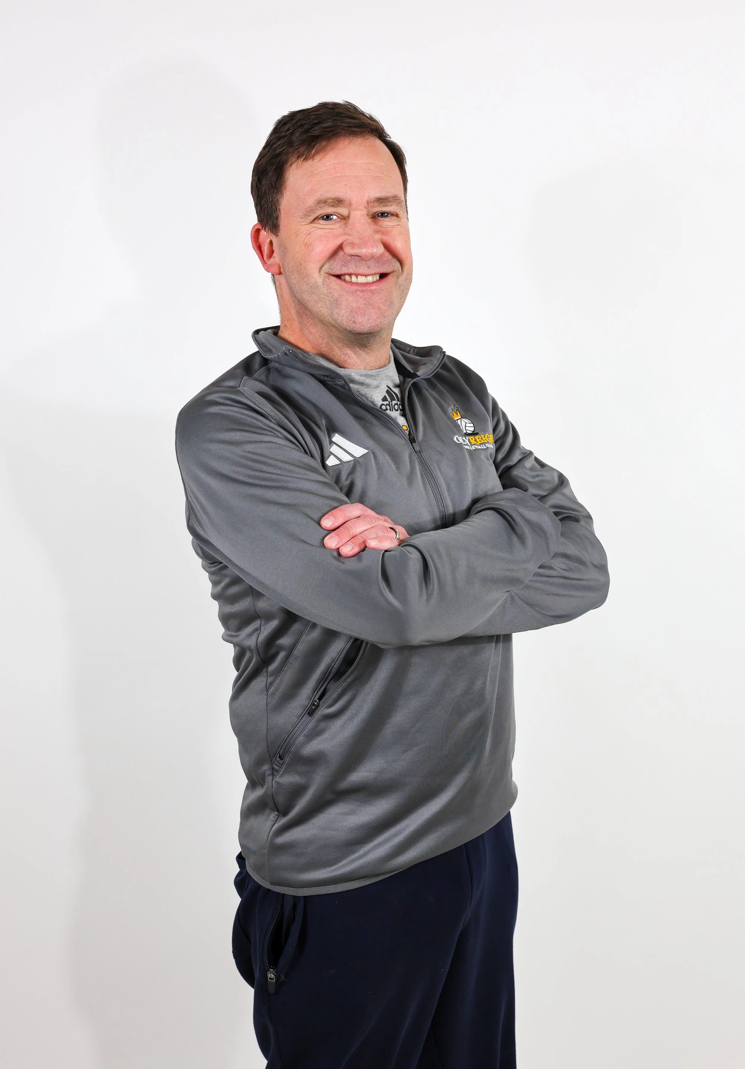 Man in athletic apparel standing against a white background with arms crossed, smiling at the camera.