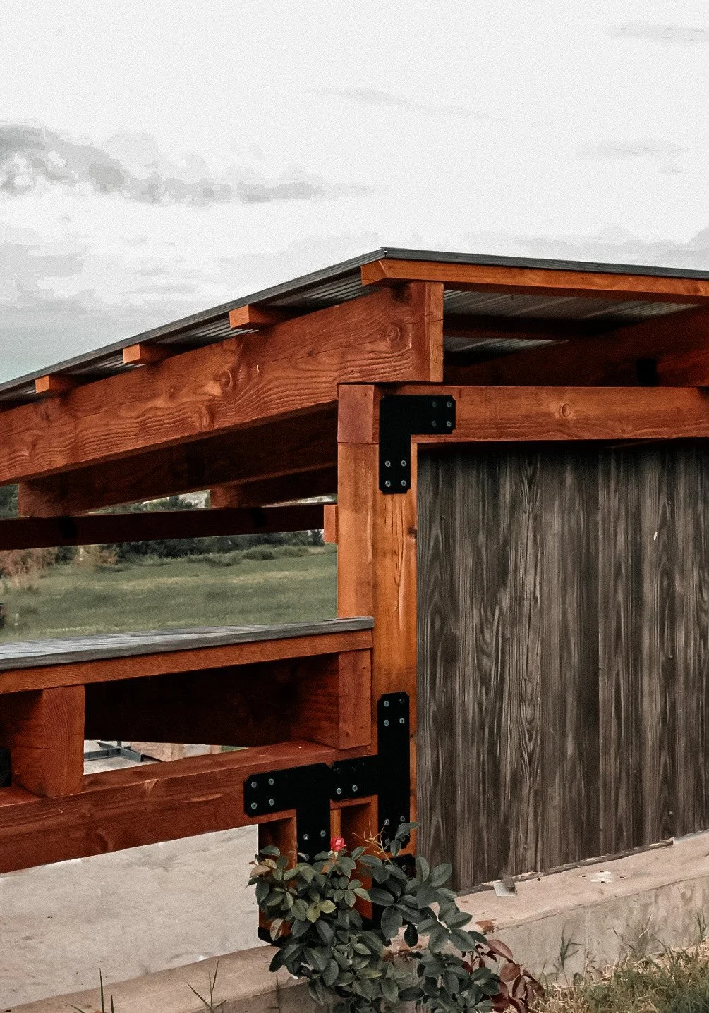 Close-up of a wooden structure with black metal brackets, part of a deck or porch, against a natural landscape background.
