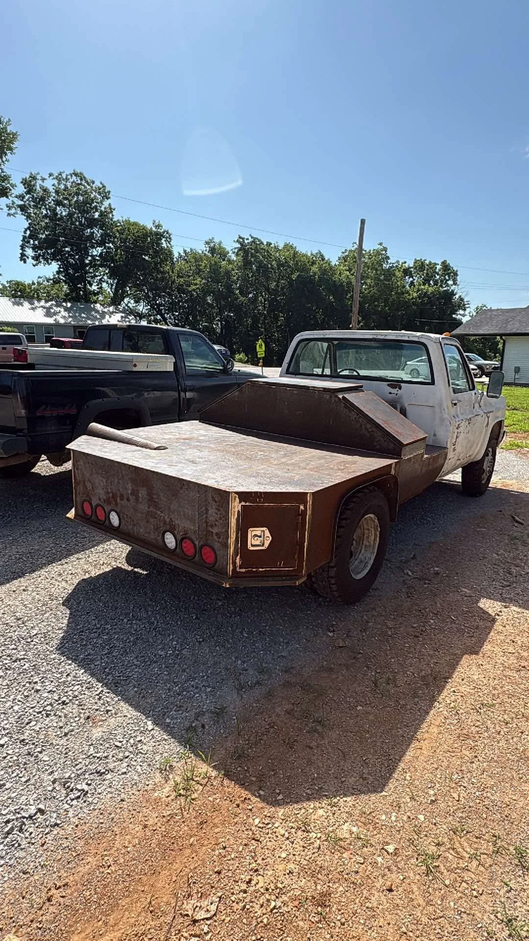 A pickup truck with a rusted, metallic flatbed in an outdoor parking lot, with other vehicles and trees in the background.
