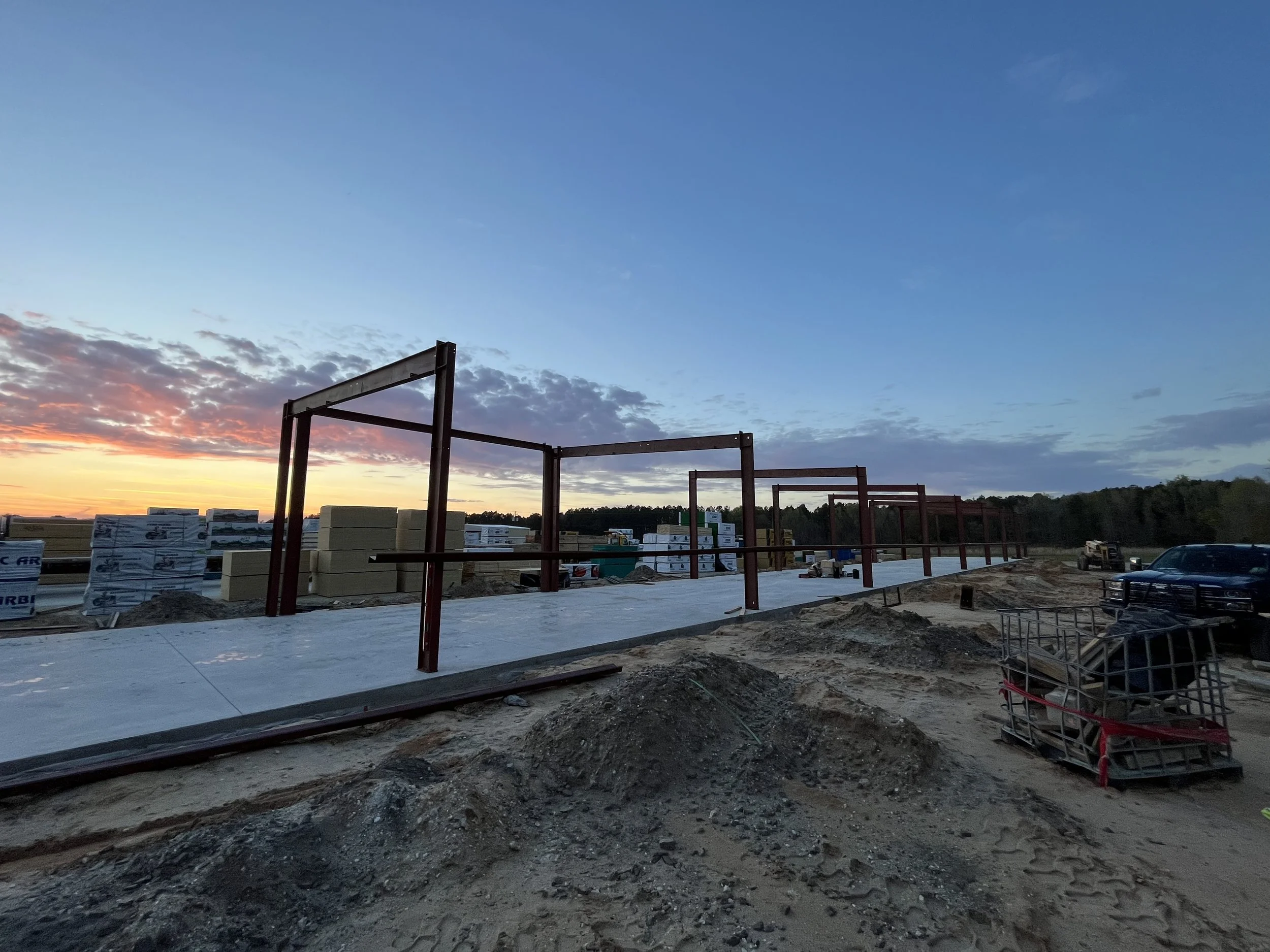 Construction site at sunset with metal framework and construction materials.
