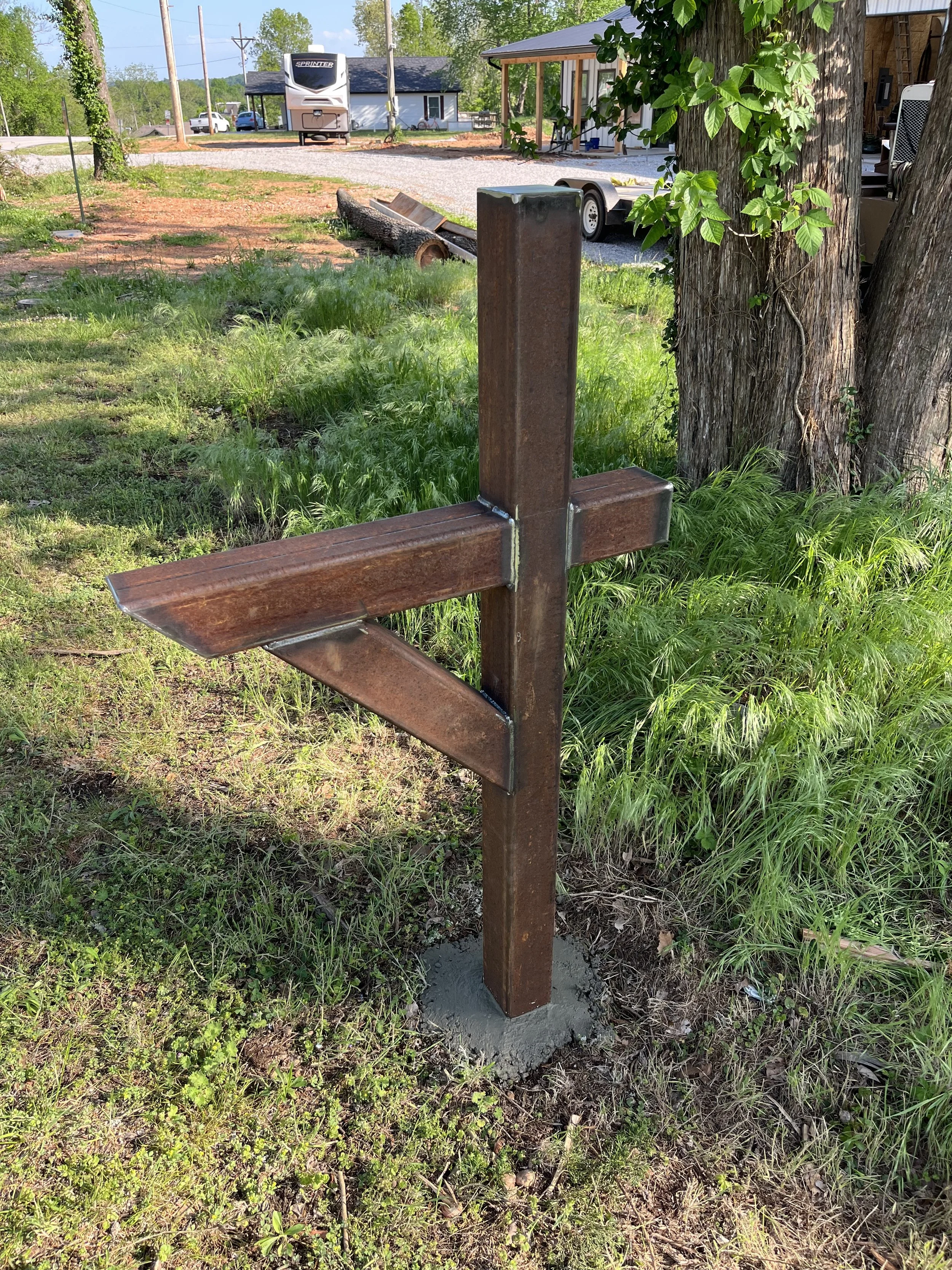 A rusty metal mail box post in a grassy outdoor area.