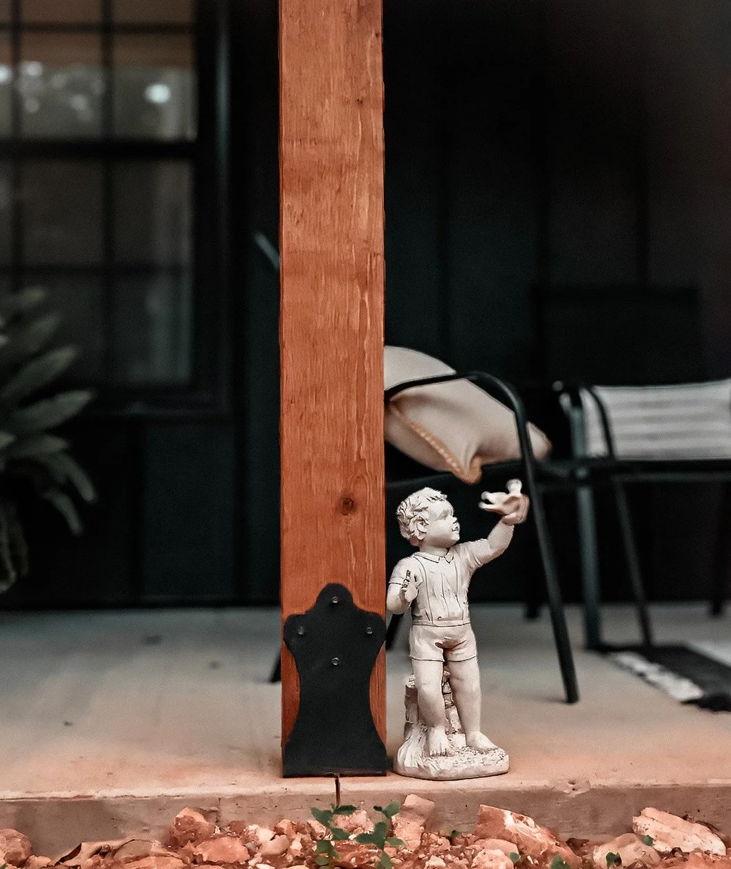 Small statue of a boy pointing, leaning against a wooden post with a 6x6 post bracket featured