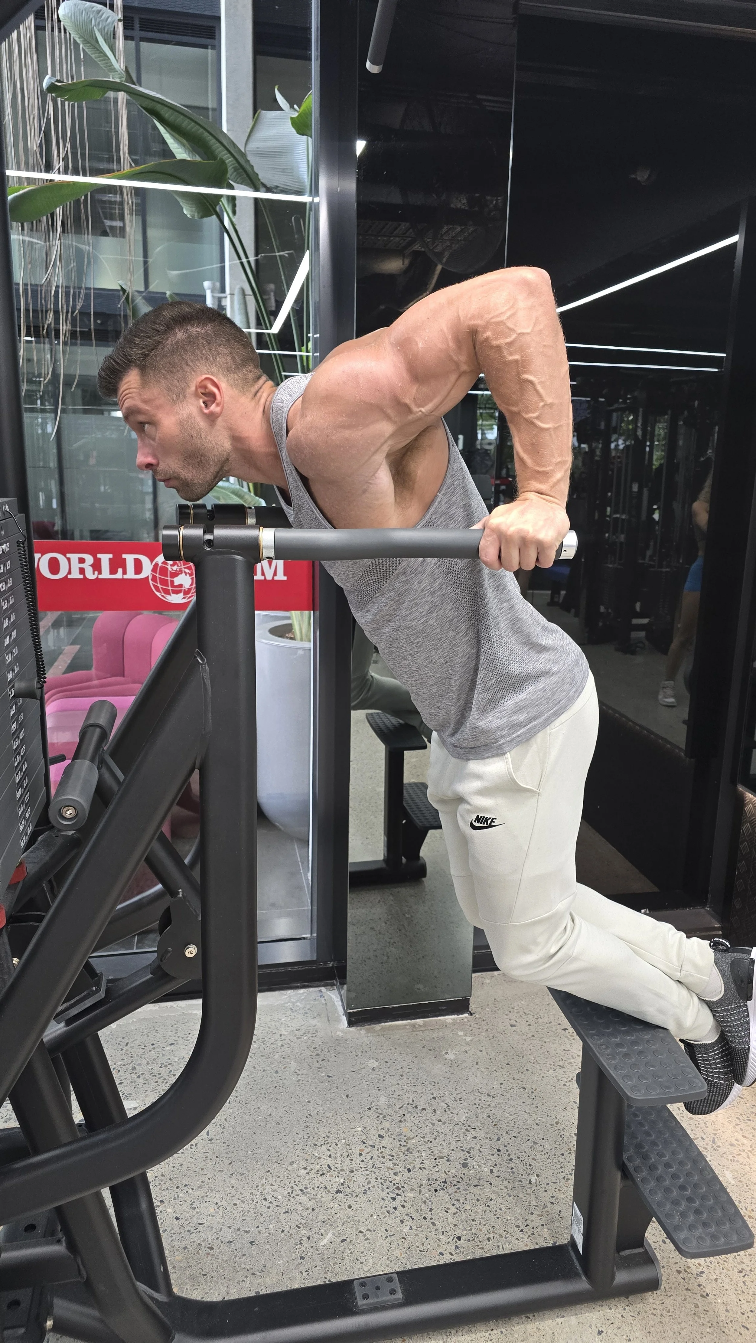 A man performing a dip exercise on parallel bars at a gym, with visible muscular arms and a focused expression.