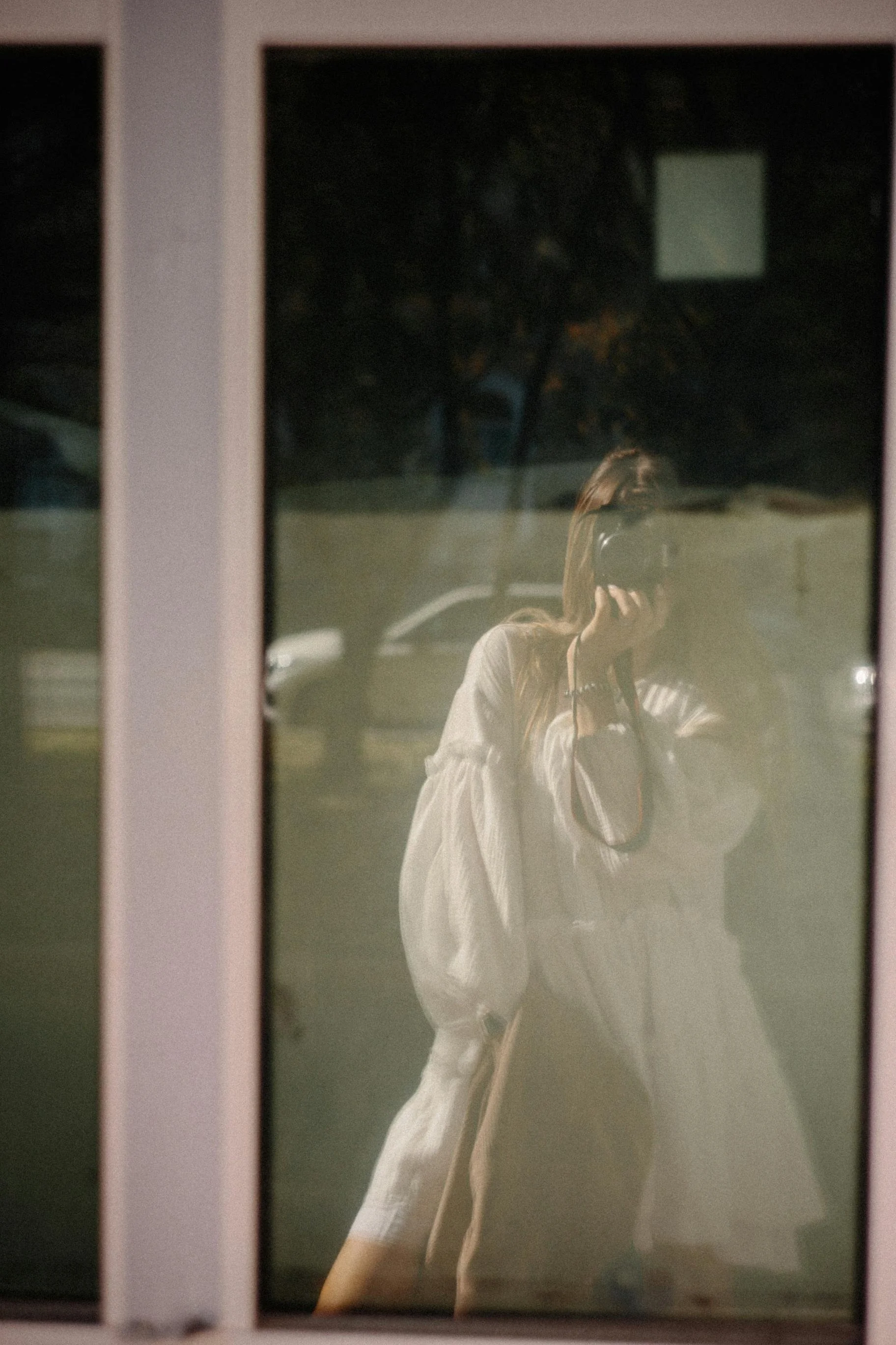 Person taking a photo of their reflection in a window at night.