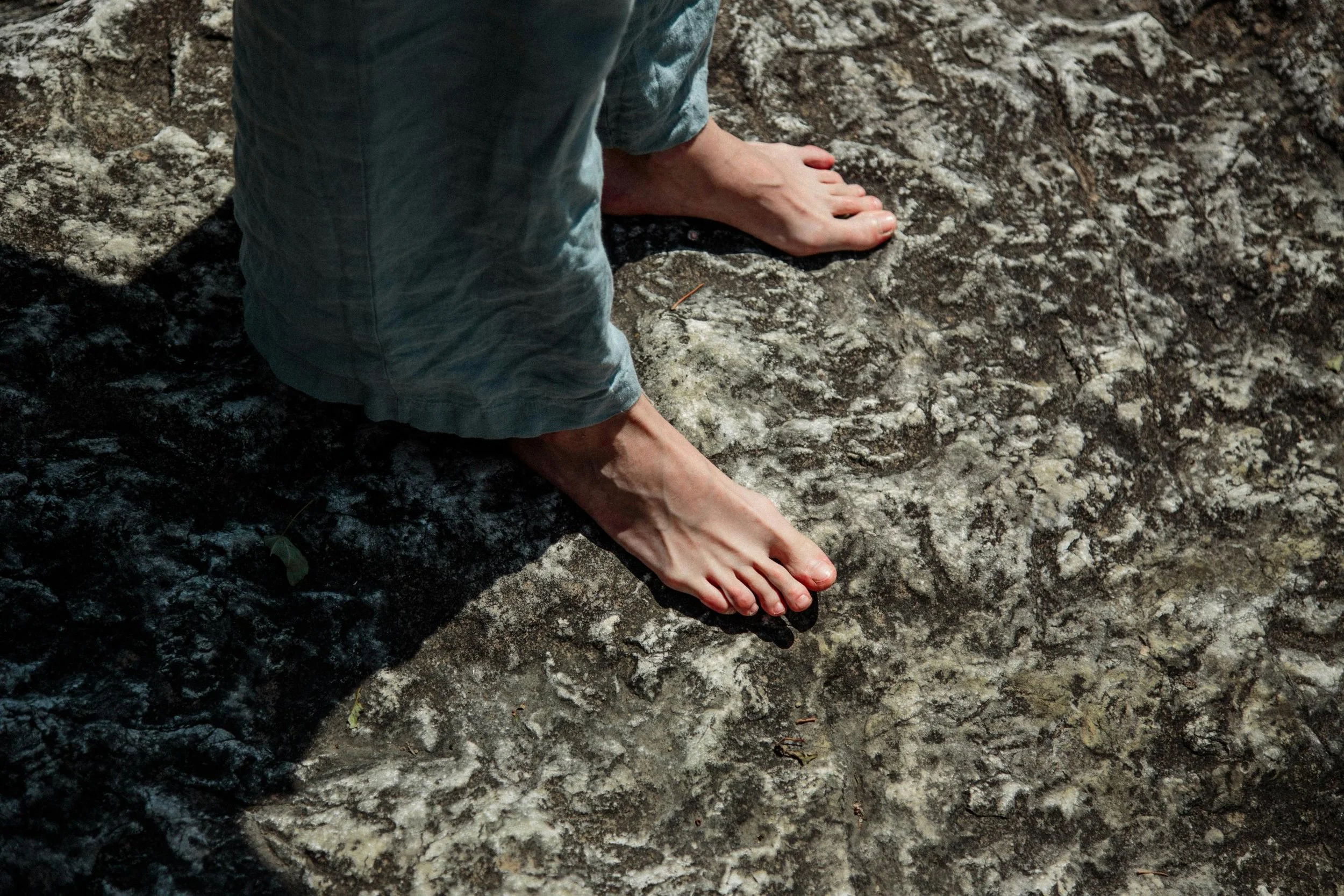 Person barefoot wearing gray pants standing on a rocky surface