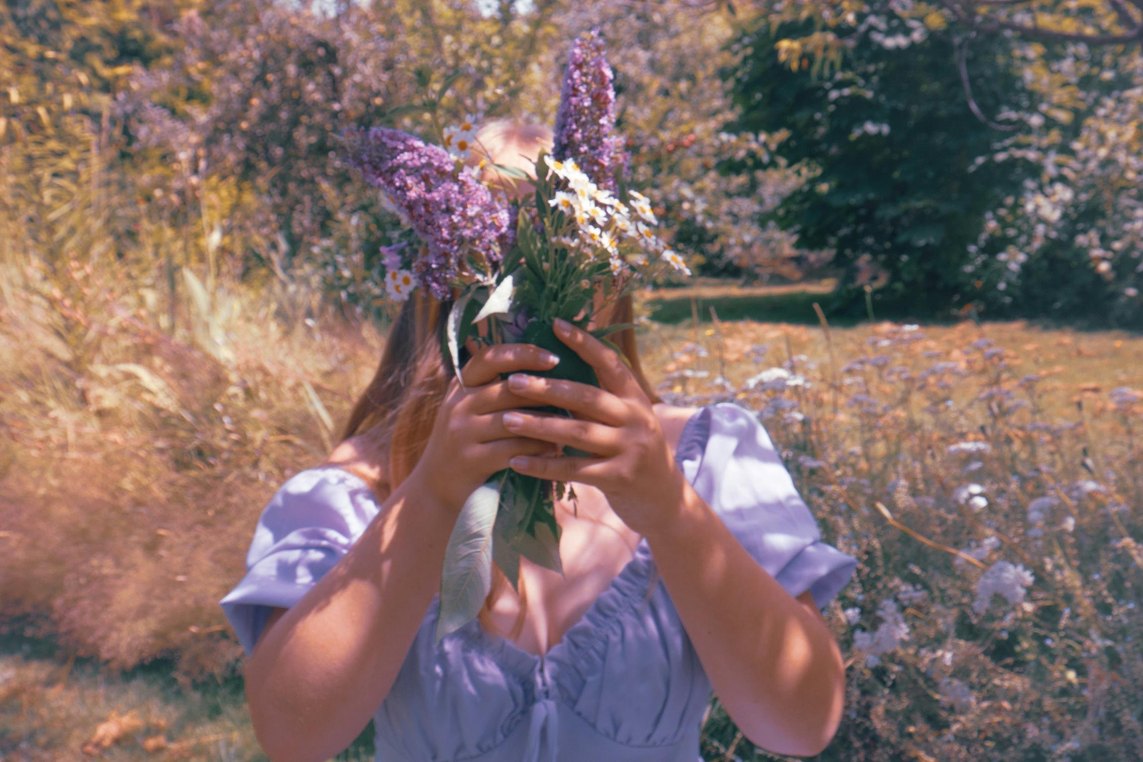 Person holding a bouquet of purple and white flowers in an outdoor setting with trees and grass.