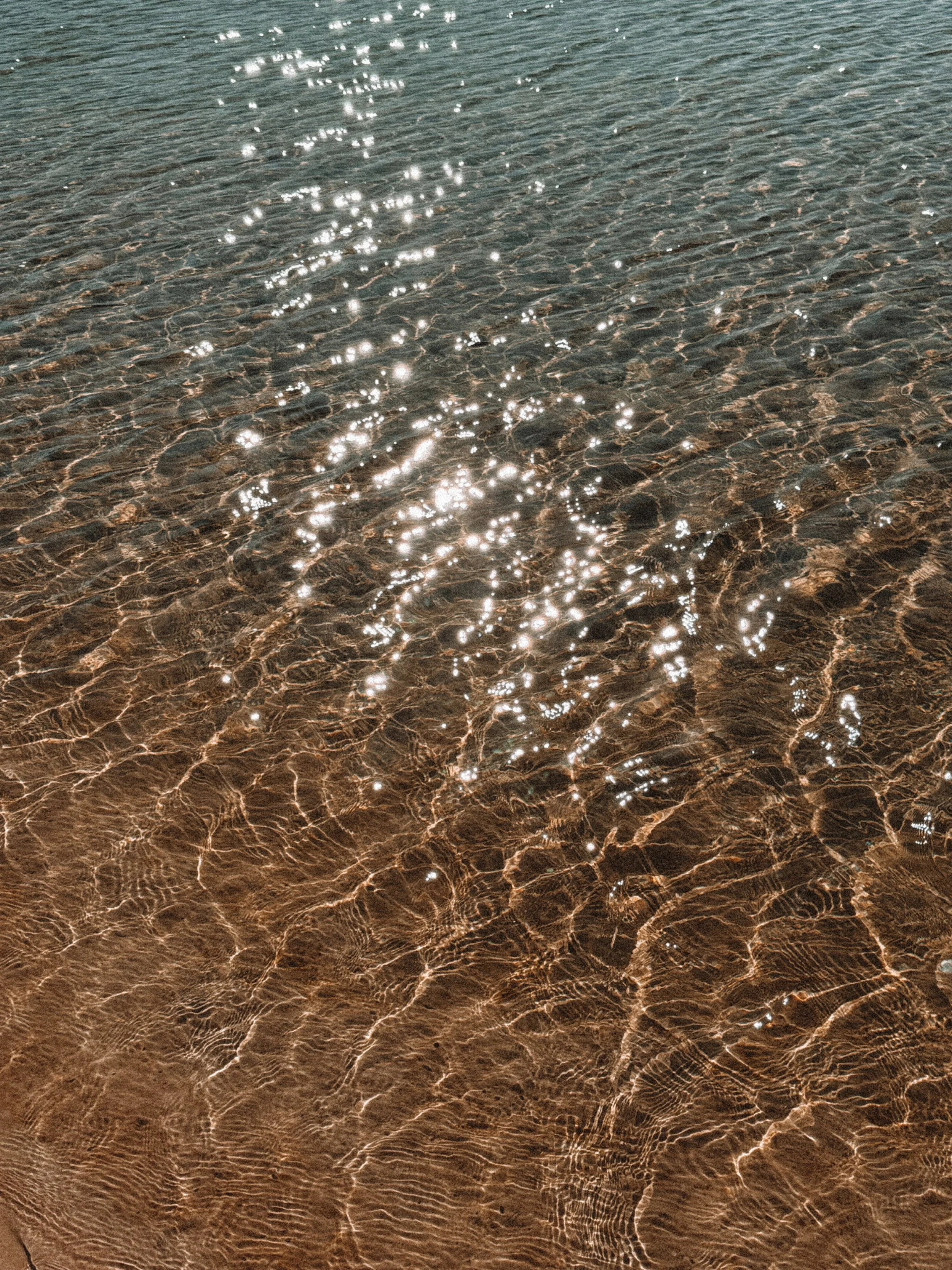 Shallow water at the beach with sunlight reflecting off the surface, creating bright sparkles on the rippling waves.