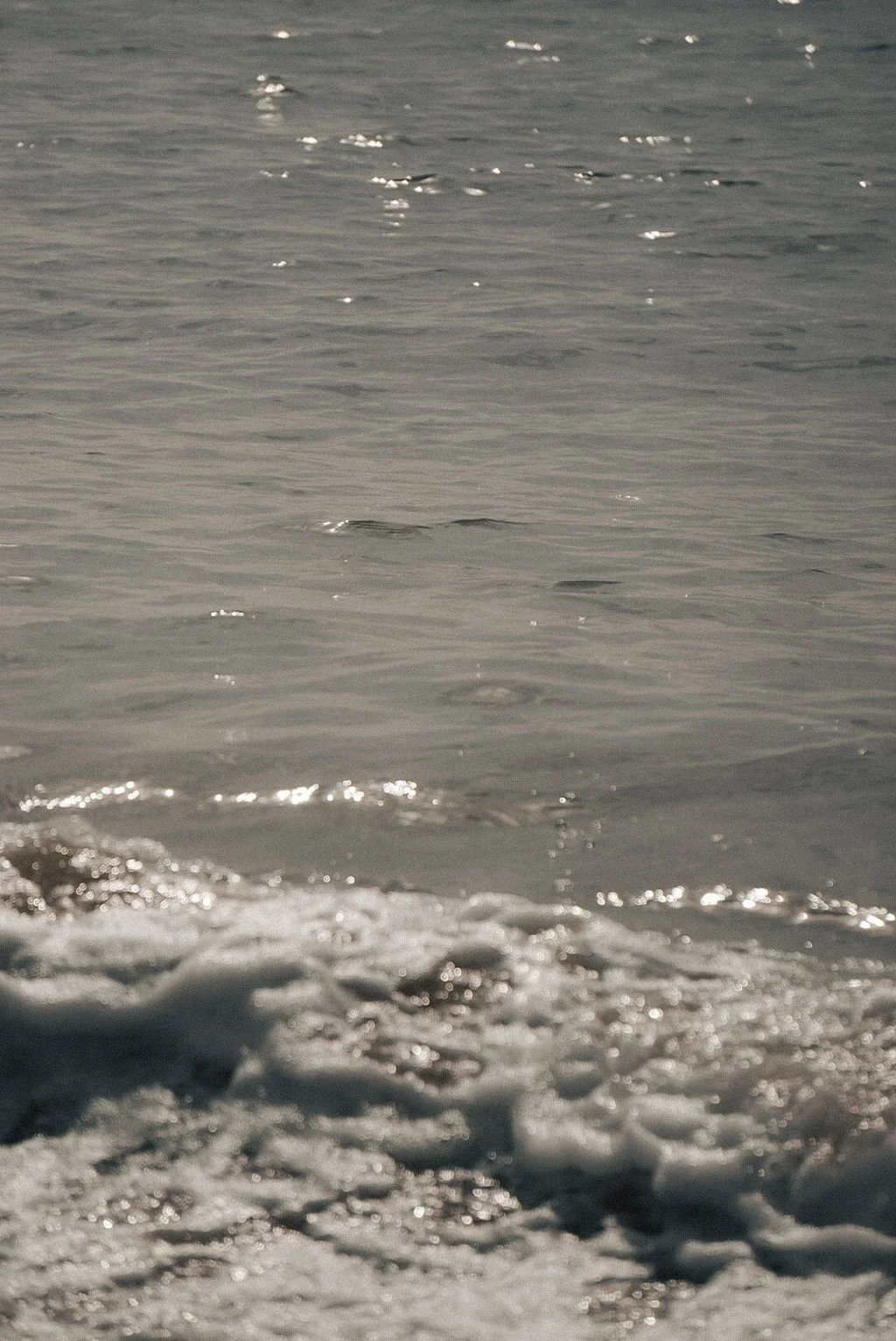 Close-up of ocean waves and foam at the shoreline during daytime.