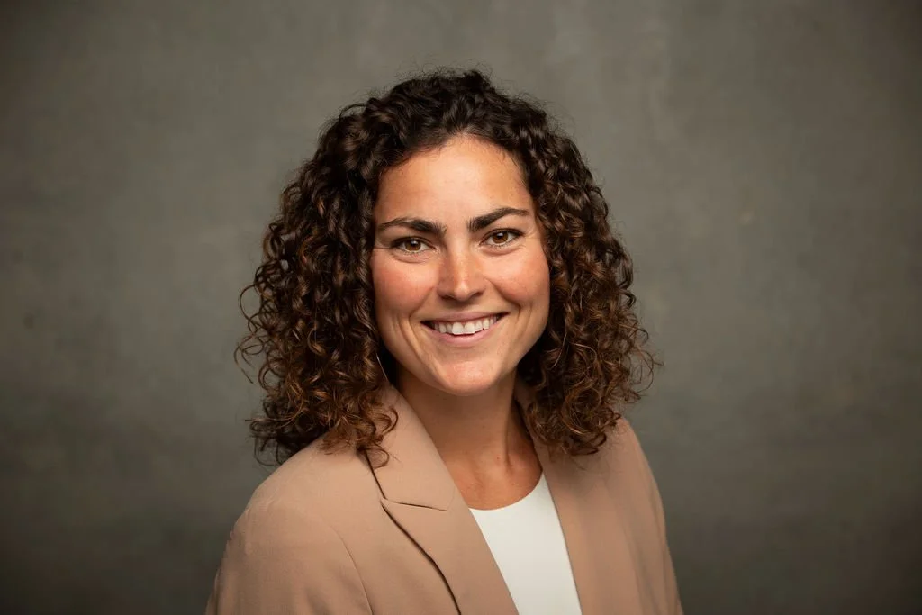 Professional headshot of Jasey Rebarcak, smiling and looking at the camera, in front of a dark green background.