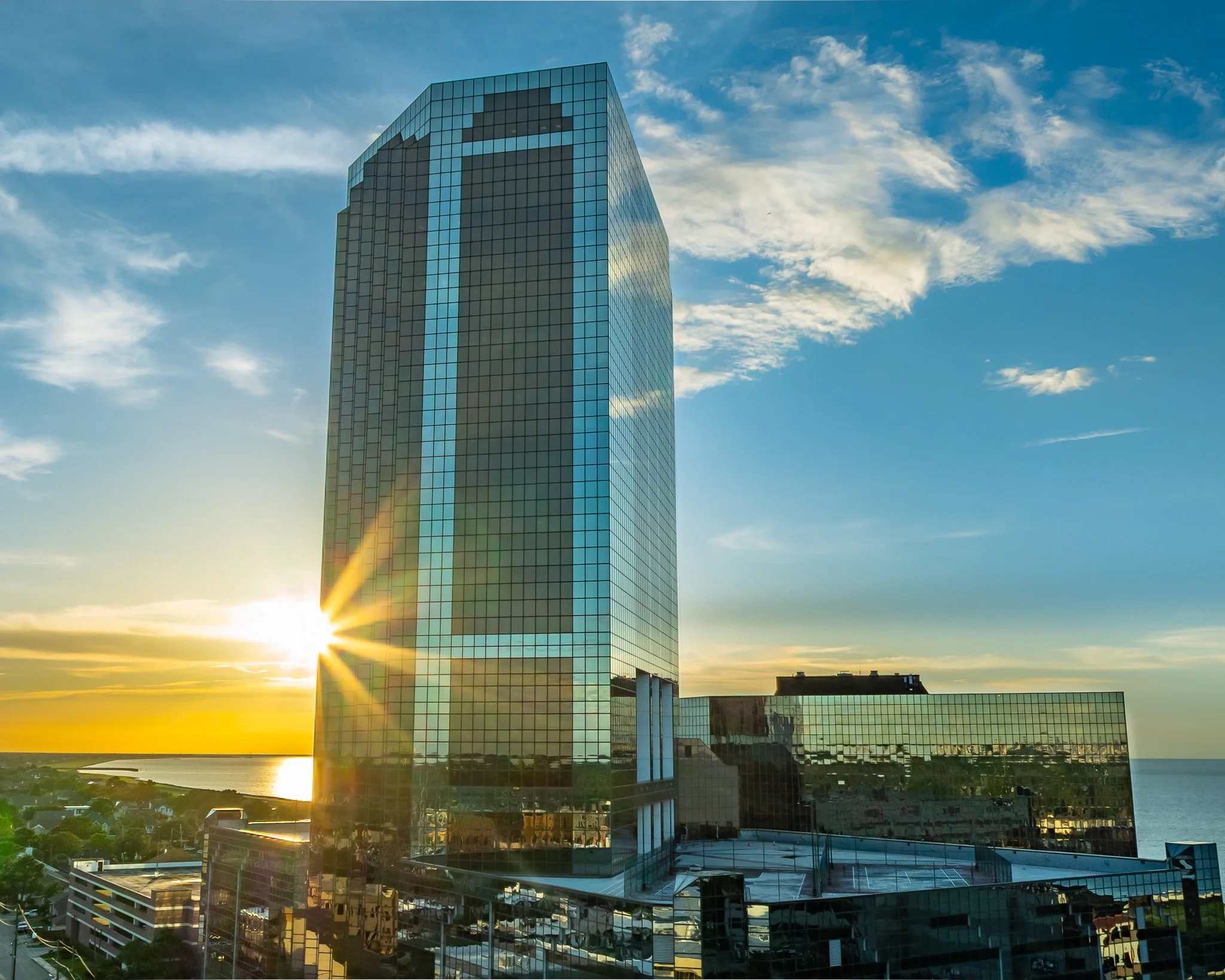 Sunset View of Metairie High-Rise near Lake Pontchartrain

A dramatic aerial perspective capturing the sun flaring behind a sleek, glass skyscraper near the shores of Lake Pontchartrain. Set against a warm golden-hour sky, the reflective glass façade