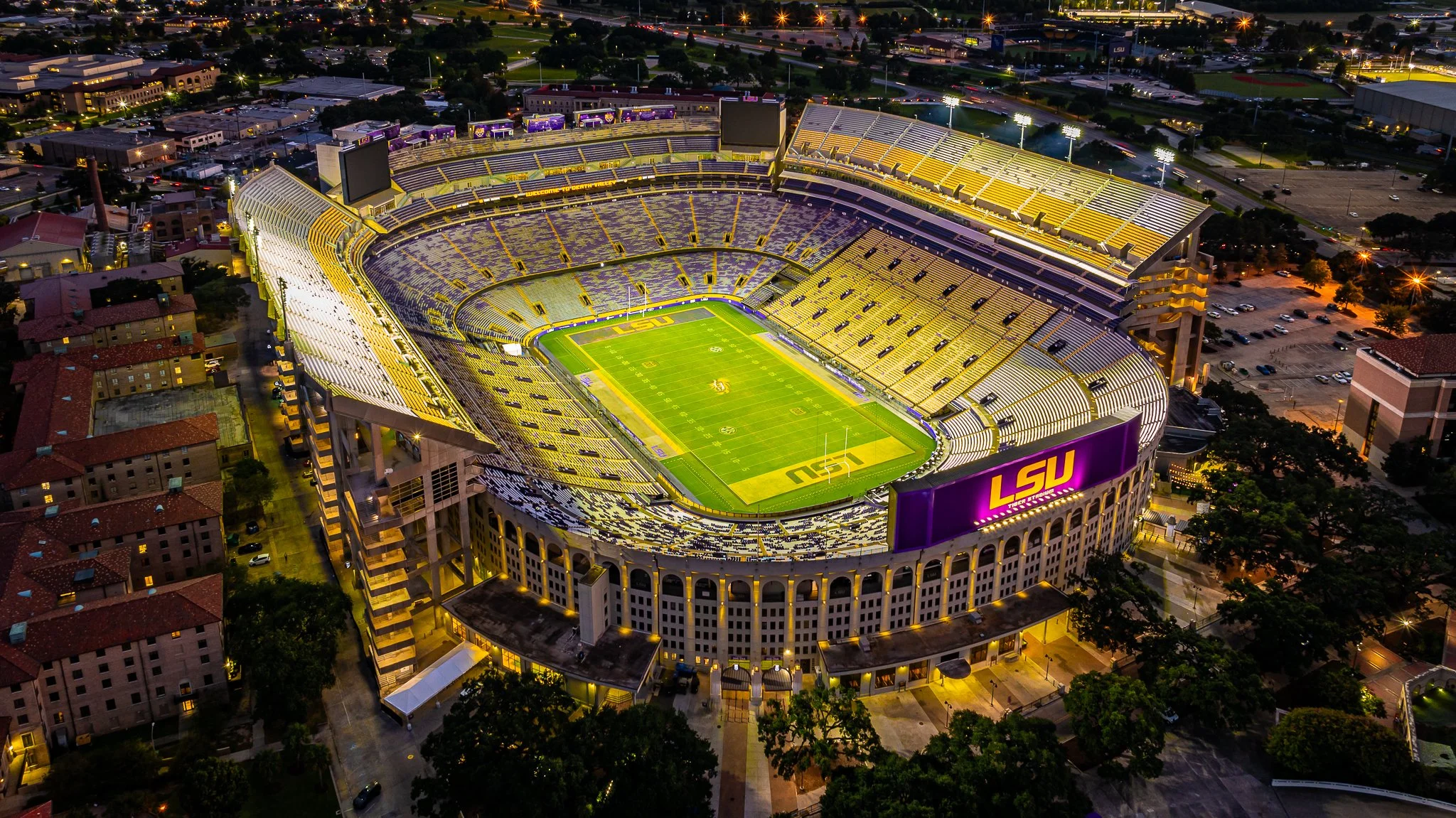 An aerial view of LSU Tiger Stadium illuminated at night, showing football field and surrounding grandstands.