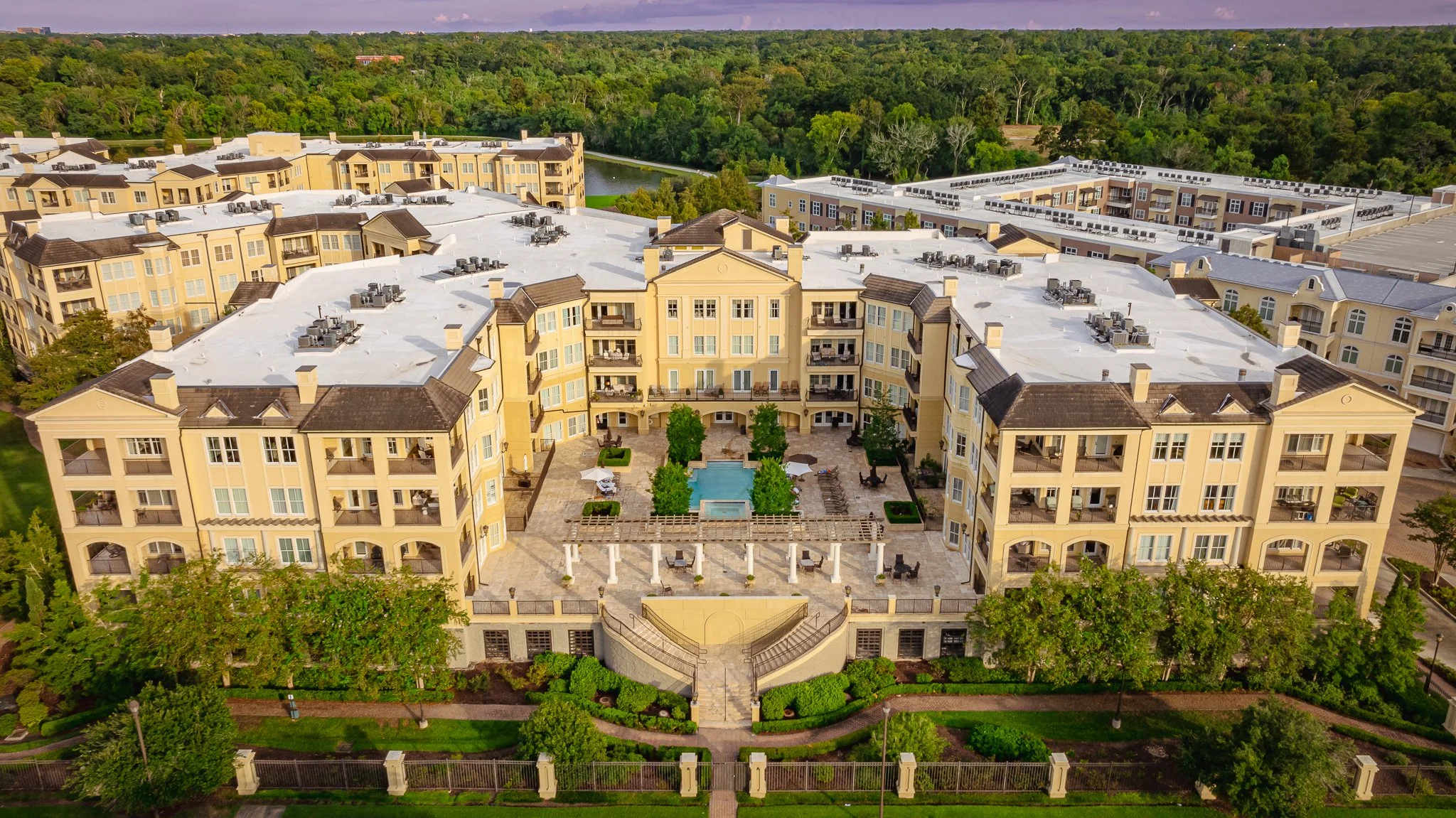 Drone view of a yellow apartment complex with a central courtyard featuring a swimming pool, surrounded by greenery and trees in Baton Rouge, LA