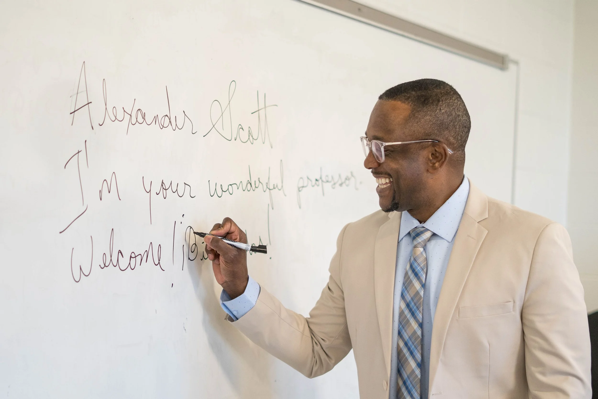 Alexander Scott writing on a whiteboard. The text on the whiteboard says "Alexander Scott. I'm your wonderful professor. Welcome! Bienvenidos!