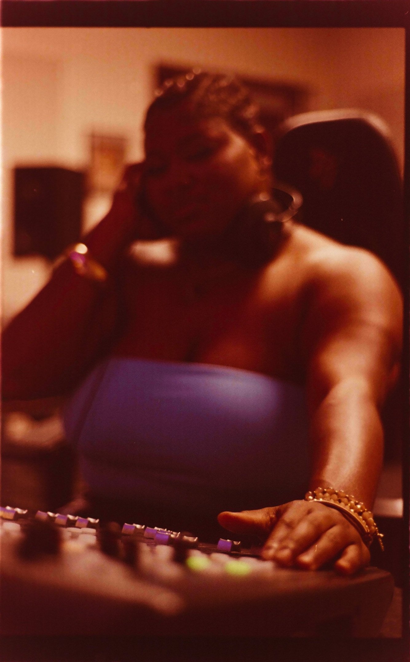 A woman with dark hair, wearing a blue strapless top, wearing gold jewelry, is operating a sound mixing console in a dimly lit room.