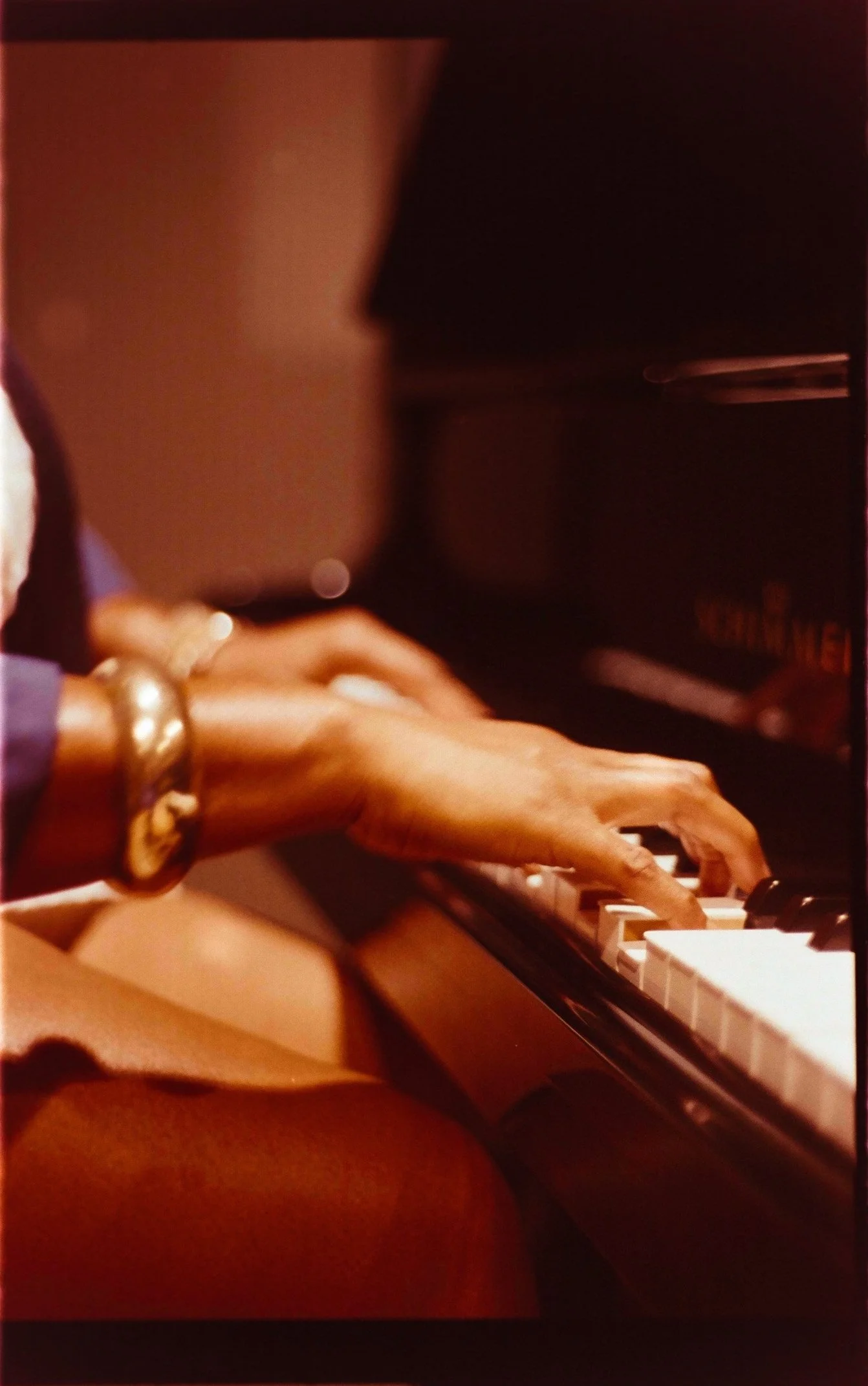 Close-up of a person's hands playing the piano, wearing multiple bracelets.