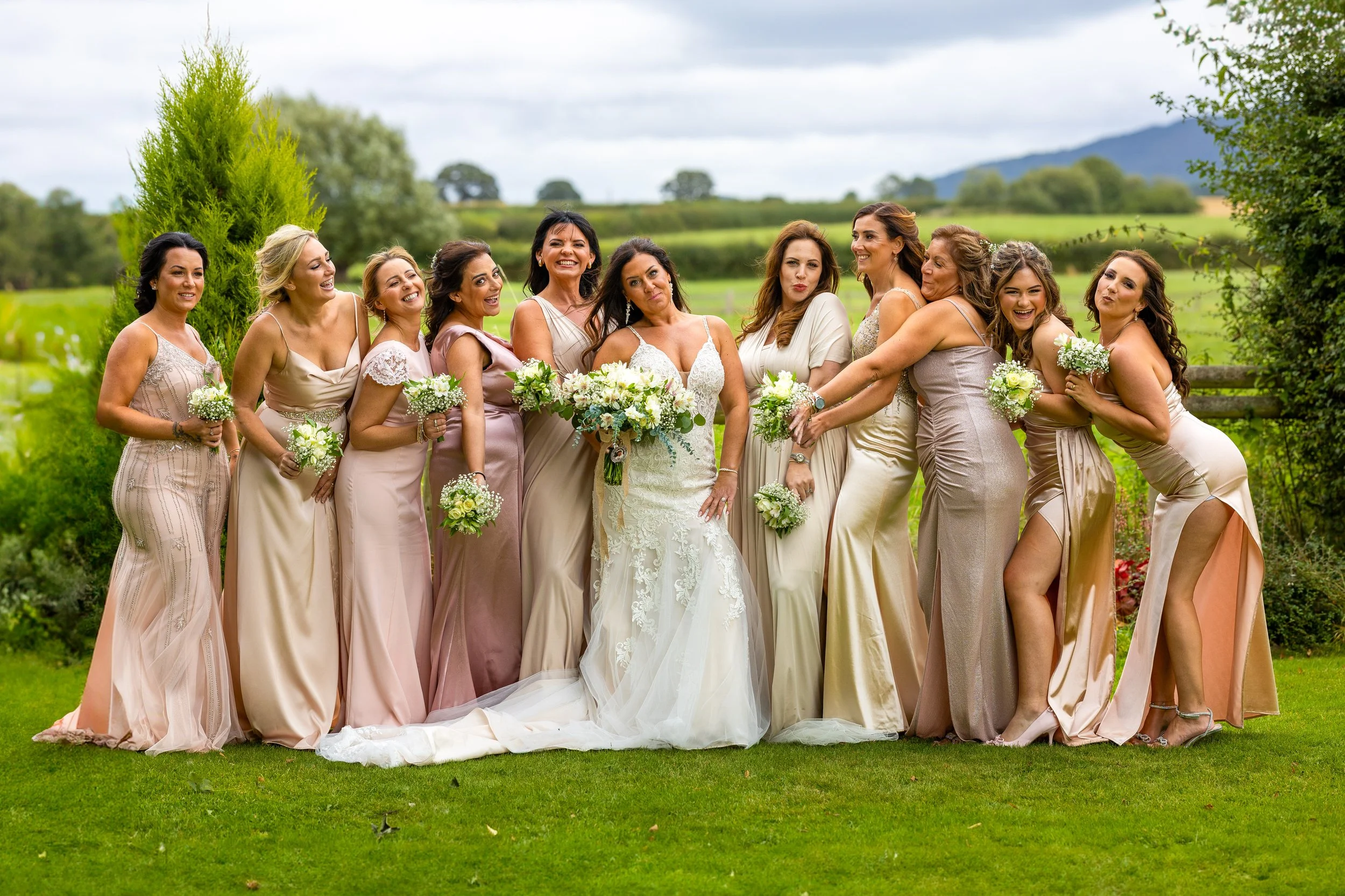 A group of women in dresses standing outdoors on a rural venue trees and The Wrekin in the background.