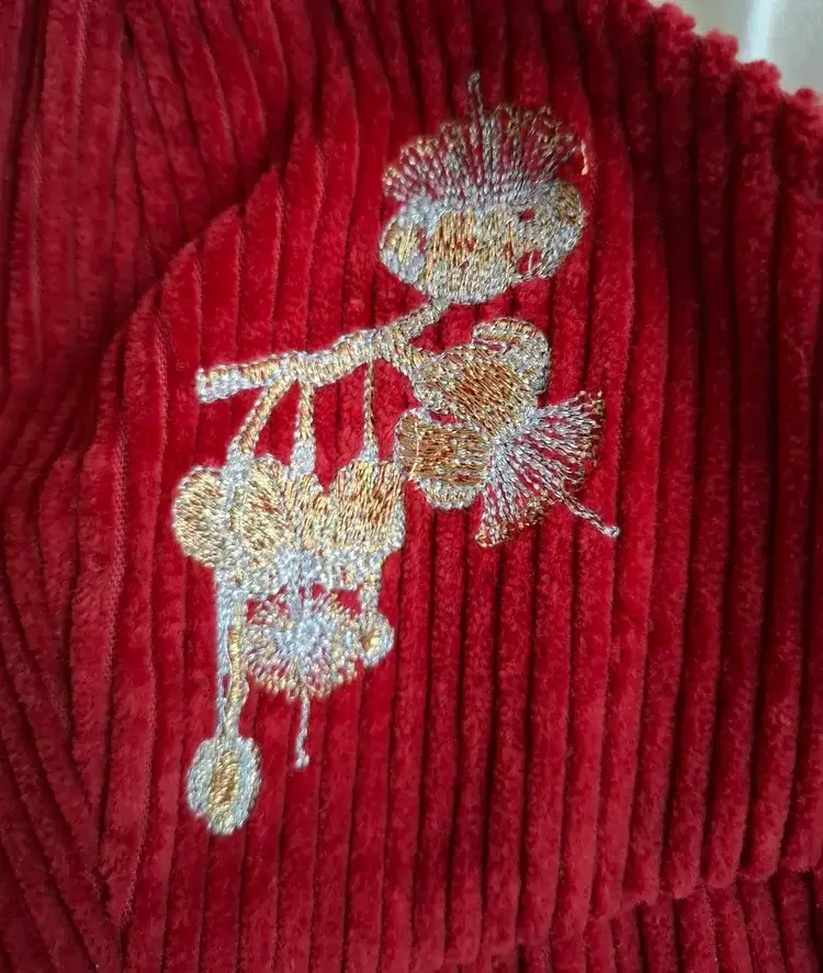 •	Close-up of embroidery details on burgundy corduroy jumpsuit