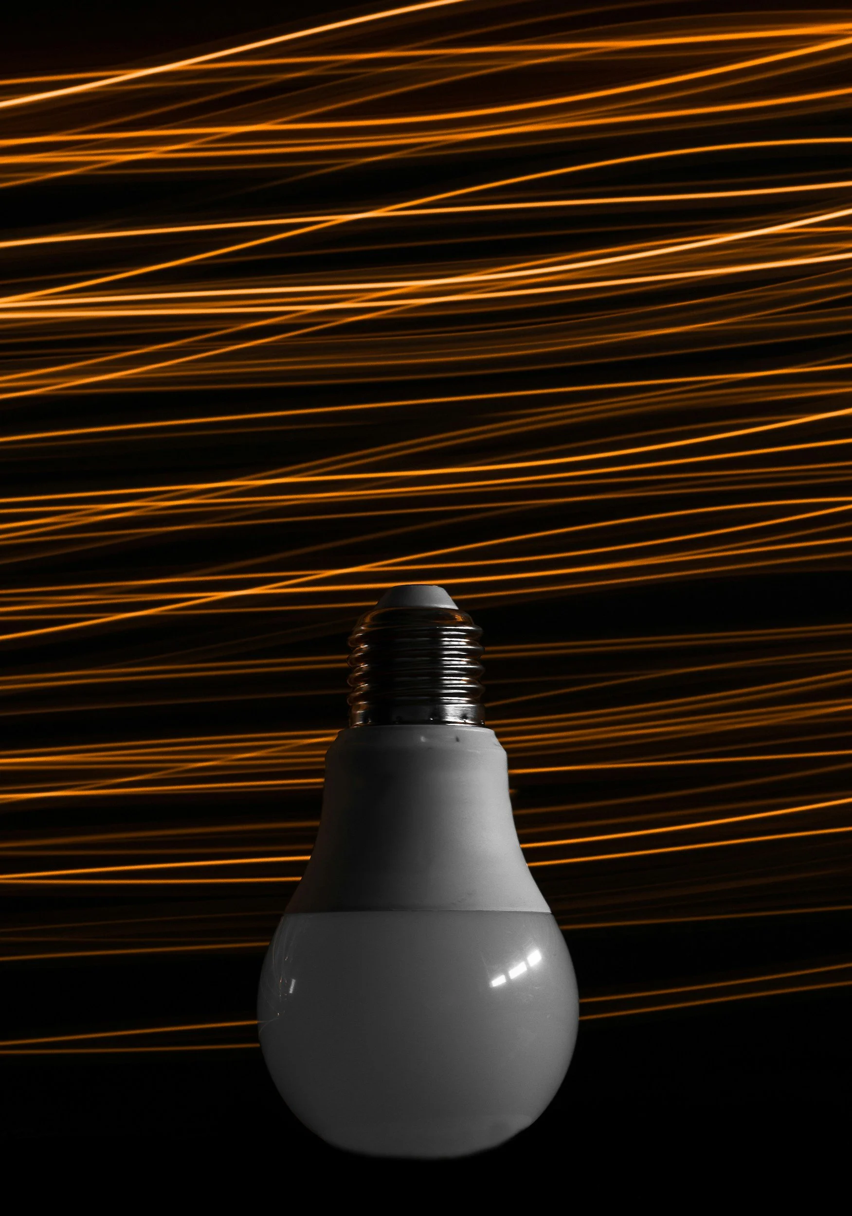 Ampoule électrique éteinte devant un fond de lignes lumineuses jaunes et oranges en mouvement.