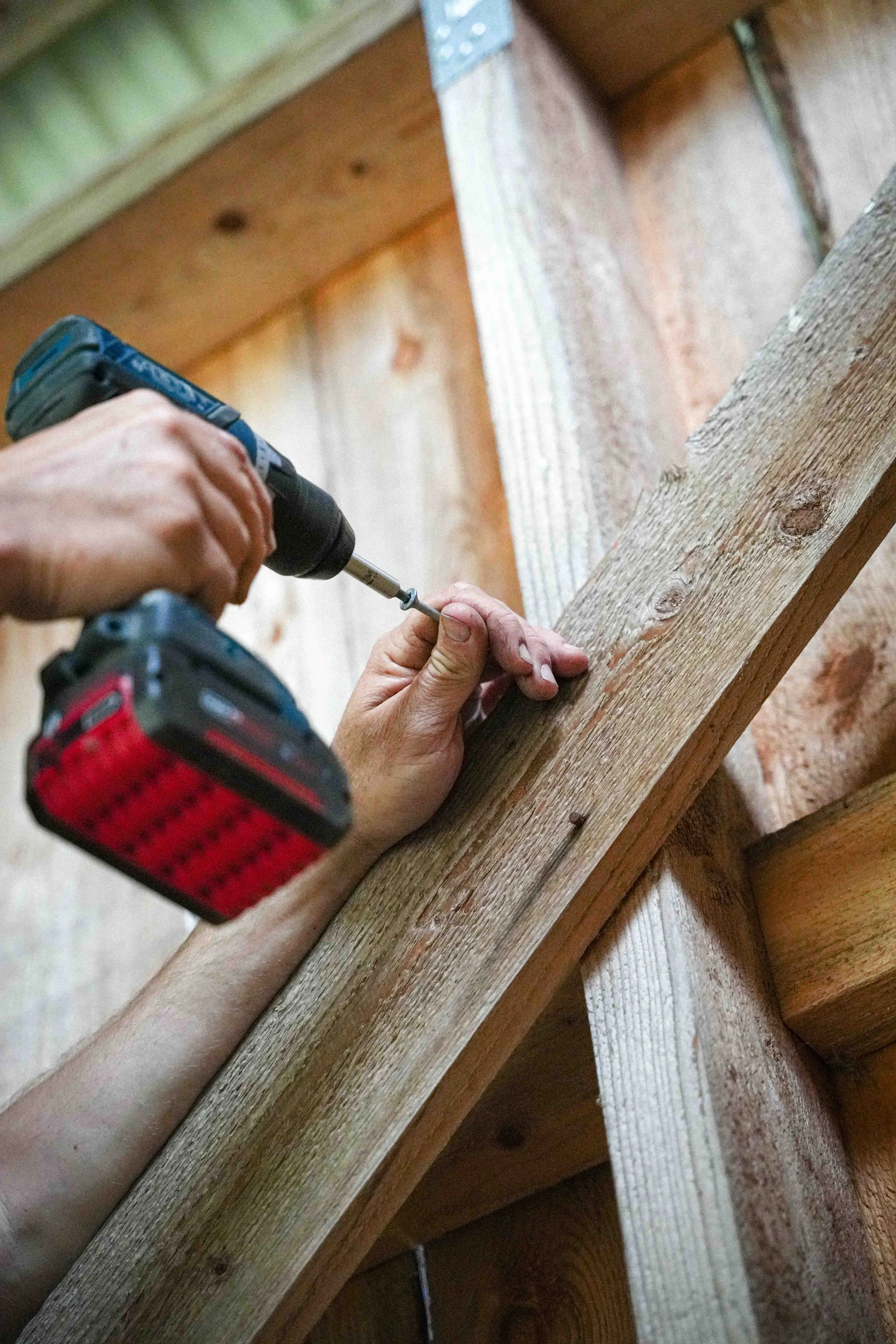 Person using a power drill to screw a piece of wood.