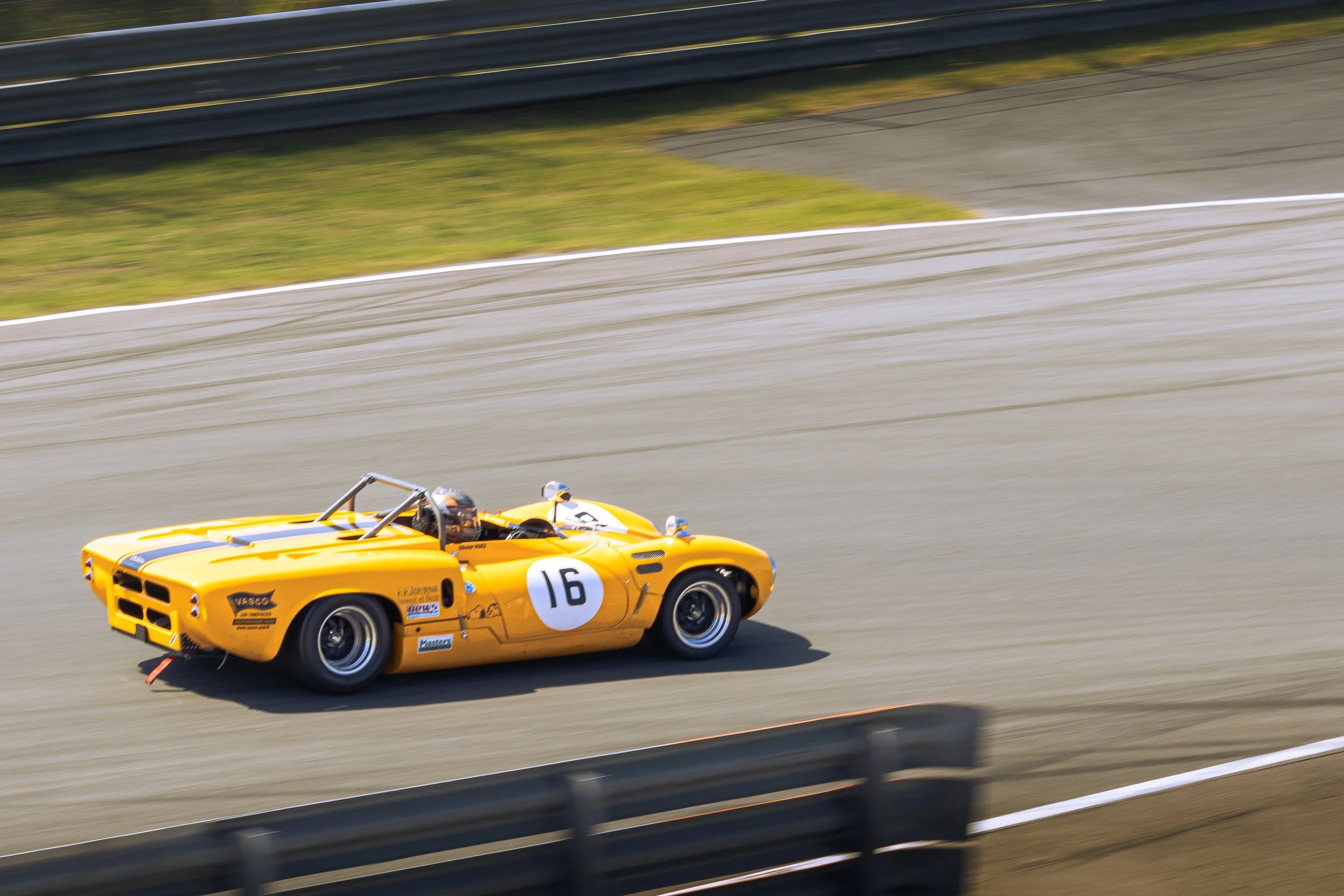 Yellow vintage race car with number 16 driving on a race track.