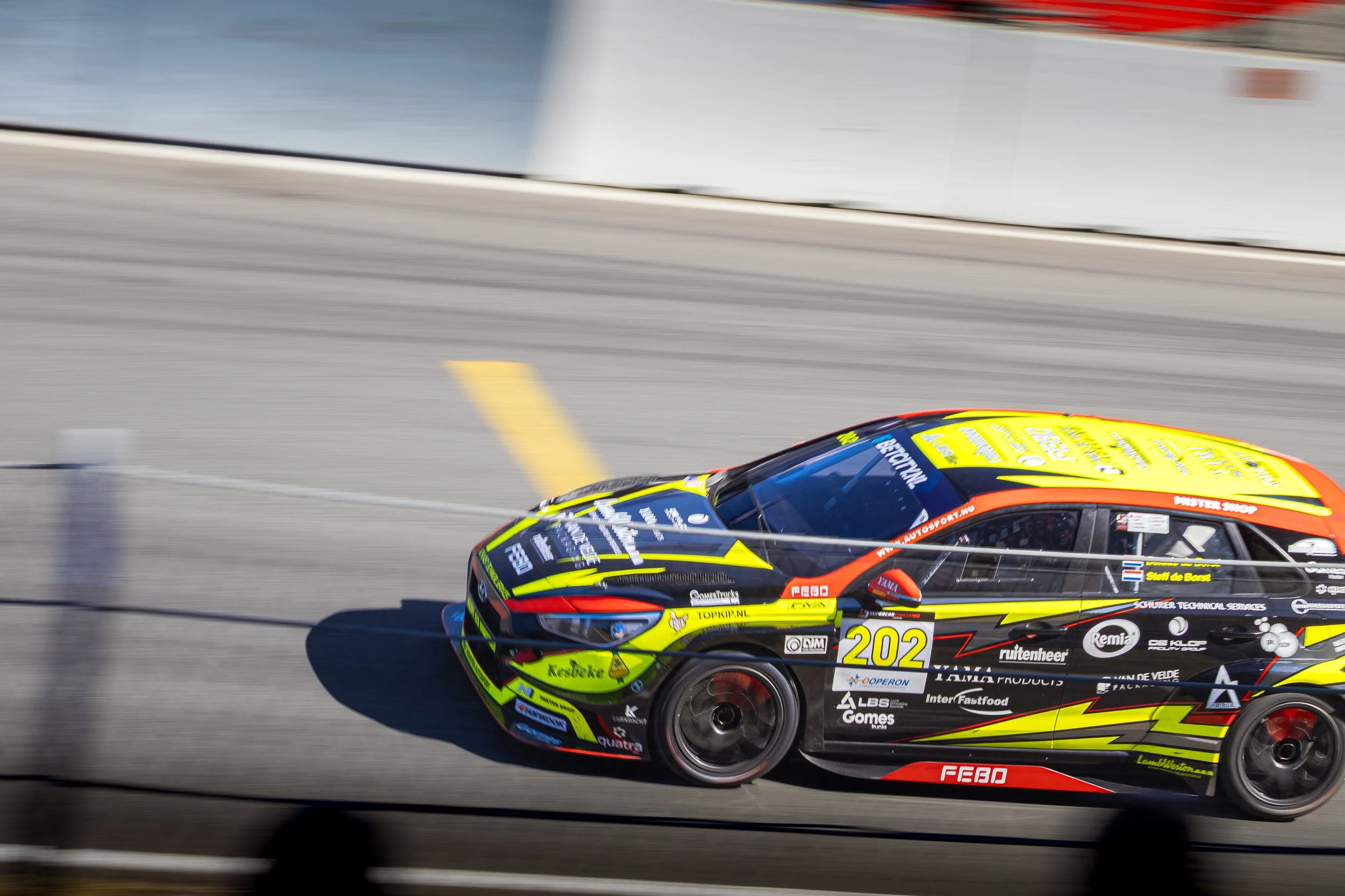 A race car with colorful sponsor decals racing on a track, showing motion blur.