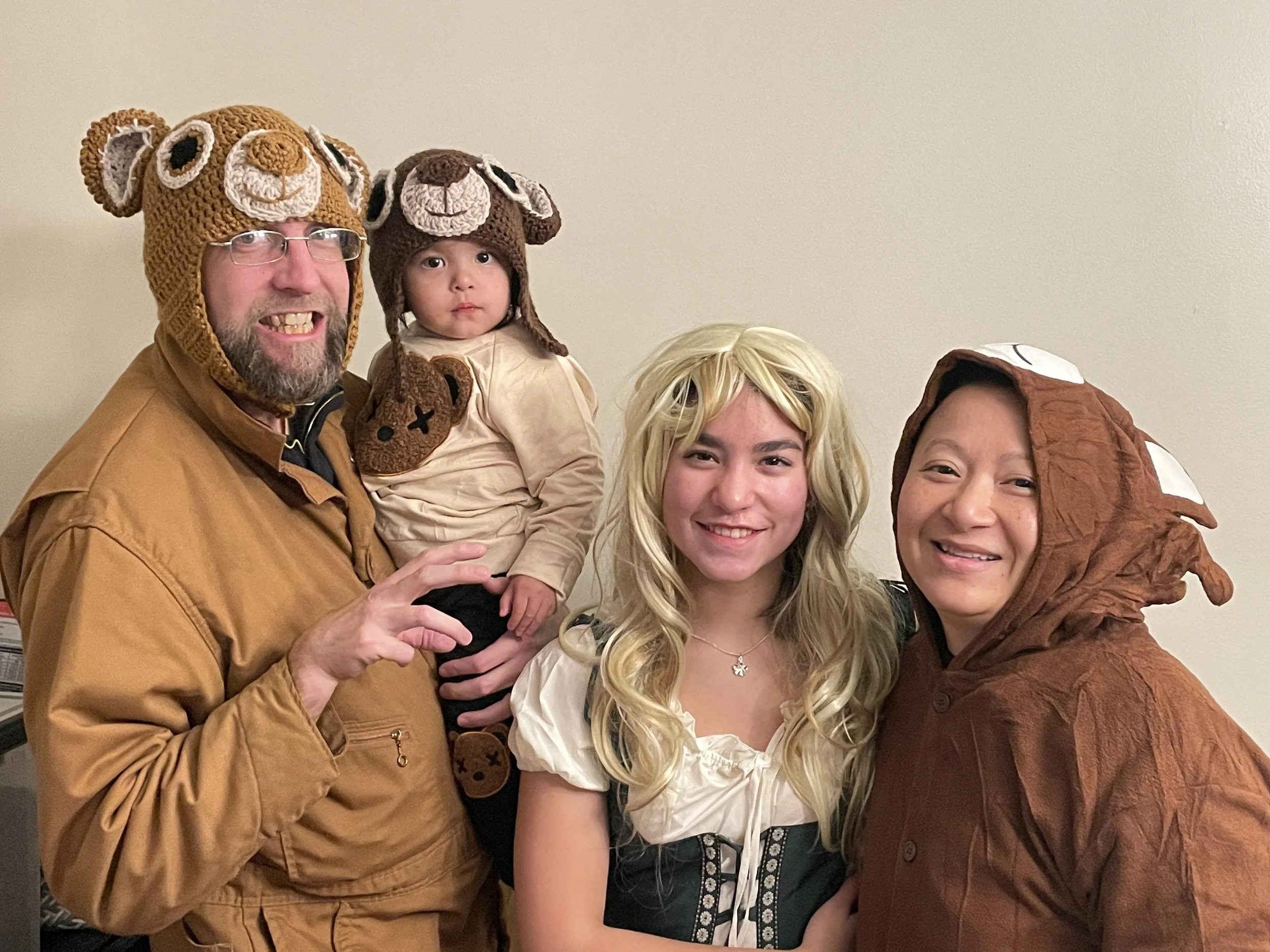 A family of four dressed in costumes with animal-themed hats, posing together indoors against a plain wall.