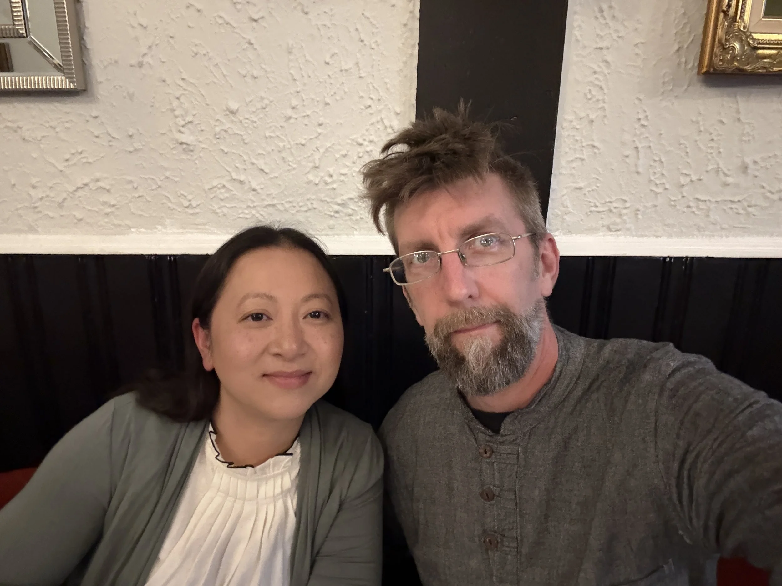 A man and woman taking a selfie together in a restaurant, both smiling at the camera.