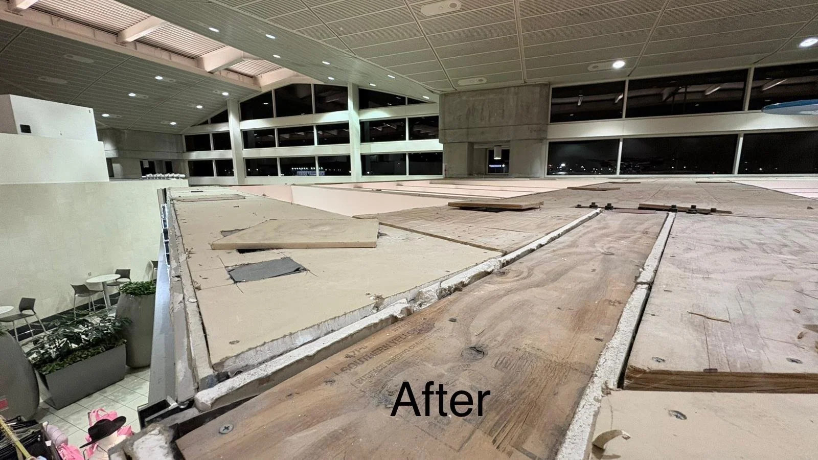 Interior of an airport or large public building under renovation, with a view of windows and exposed flooring, taken at night.