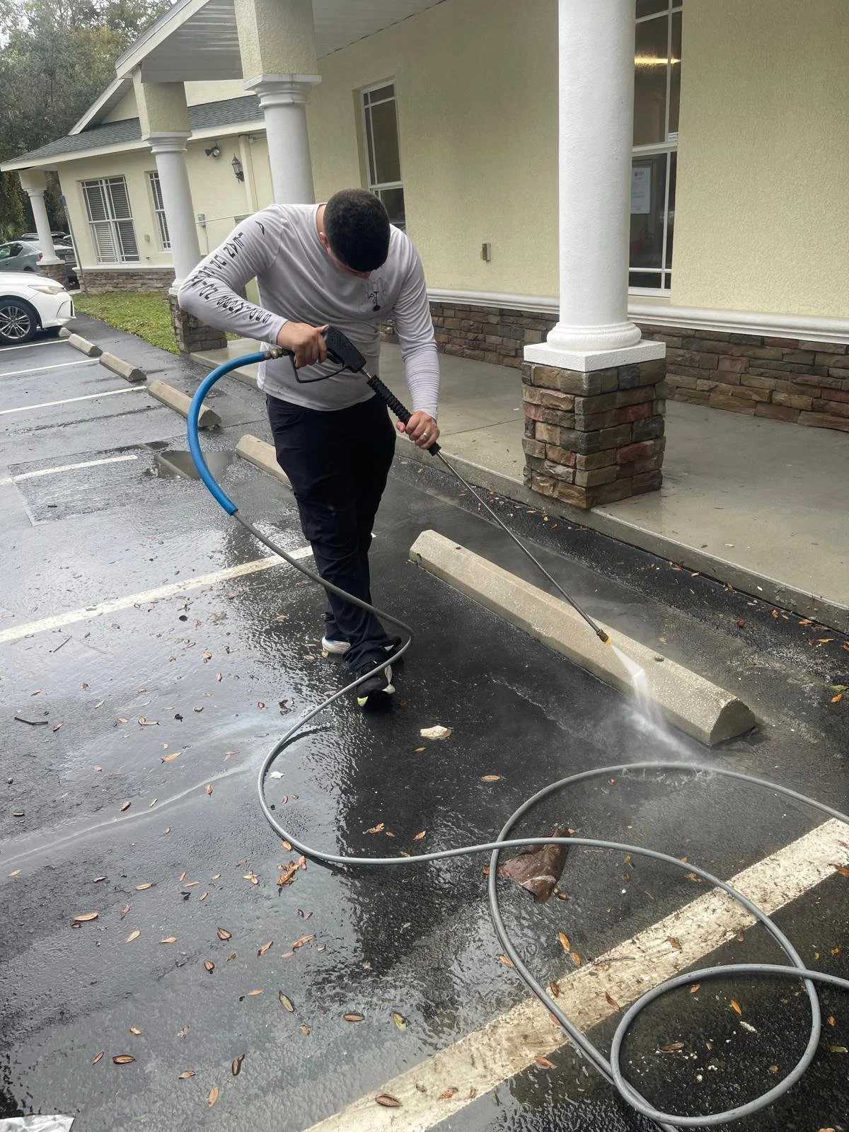 Person cleaning a parking lot with a pressure washer.