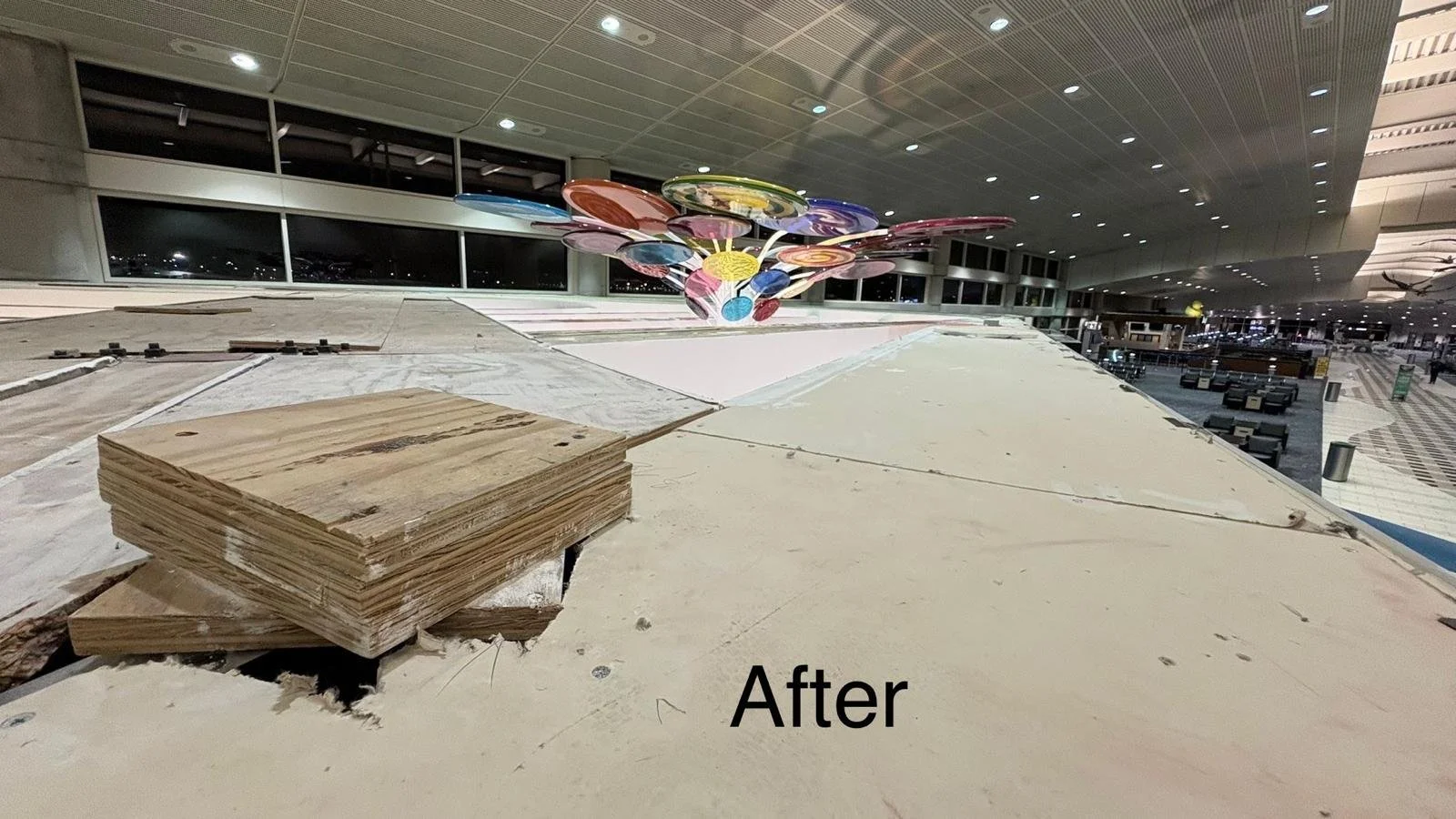 Interior of an airport terminal with construction work in progress, including stacks of plywood and a colorful ceiling decoration.