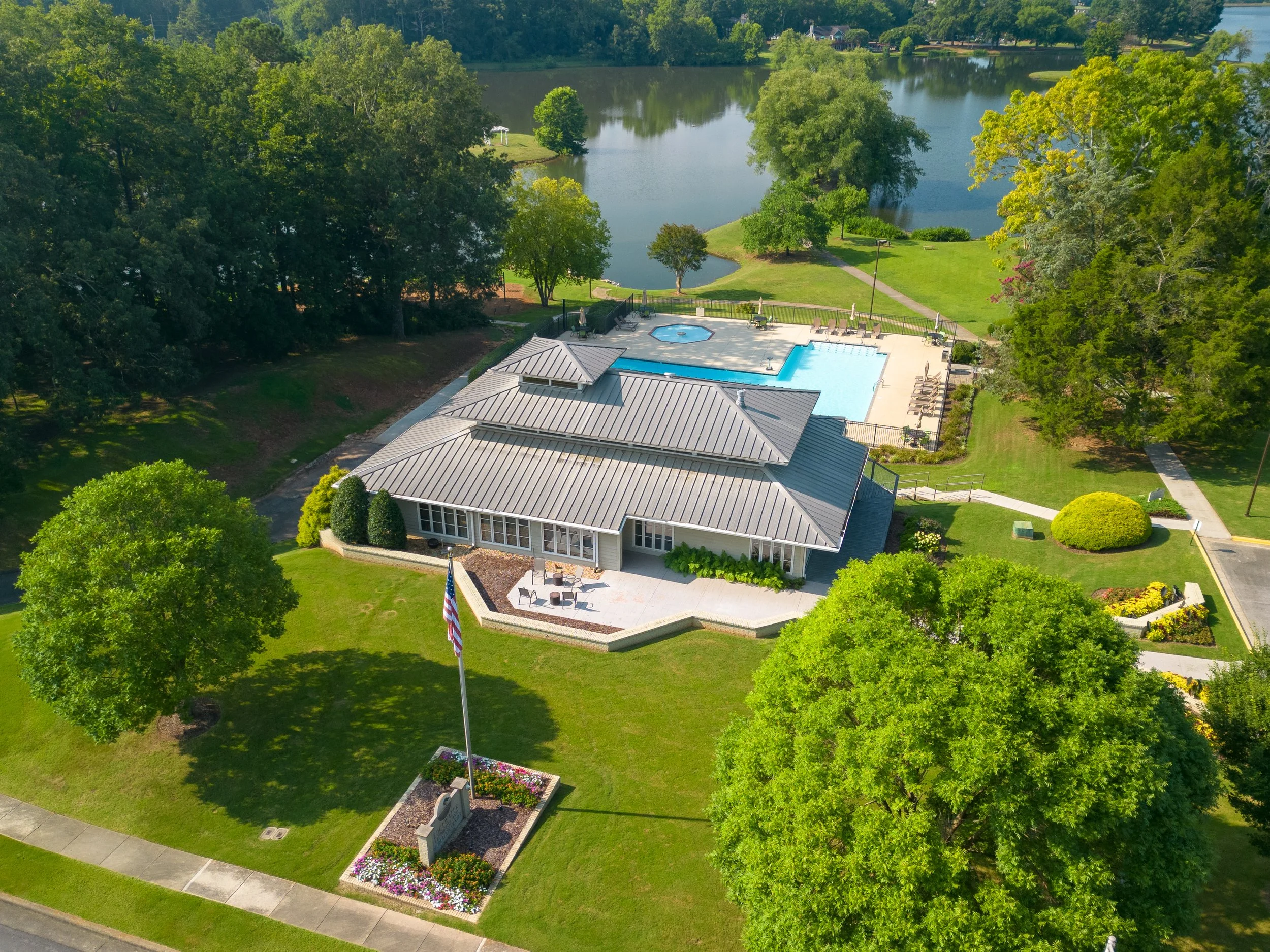 Aerial view of a house with a metal roof, a swimming pool, and surrounding greenery near a lake.