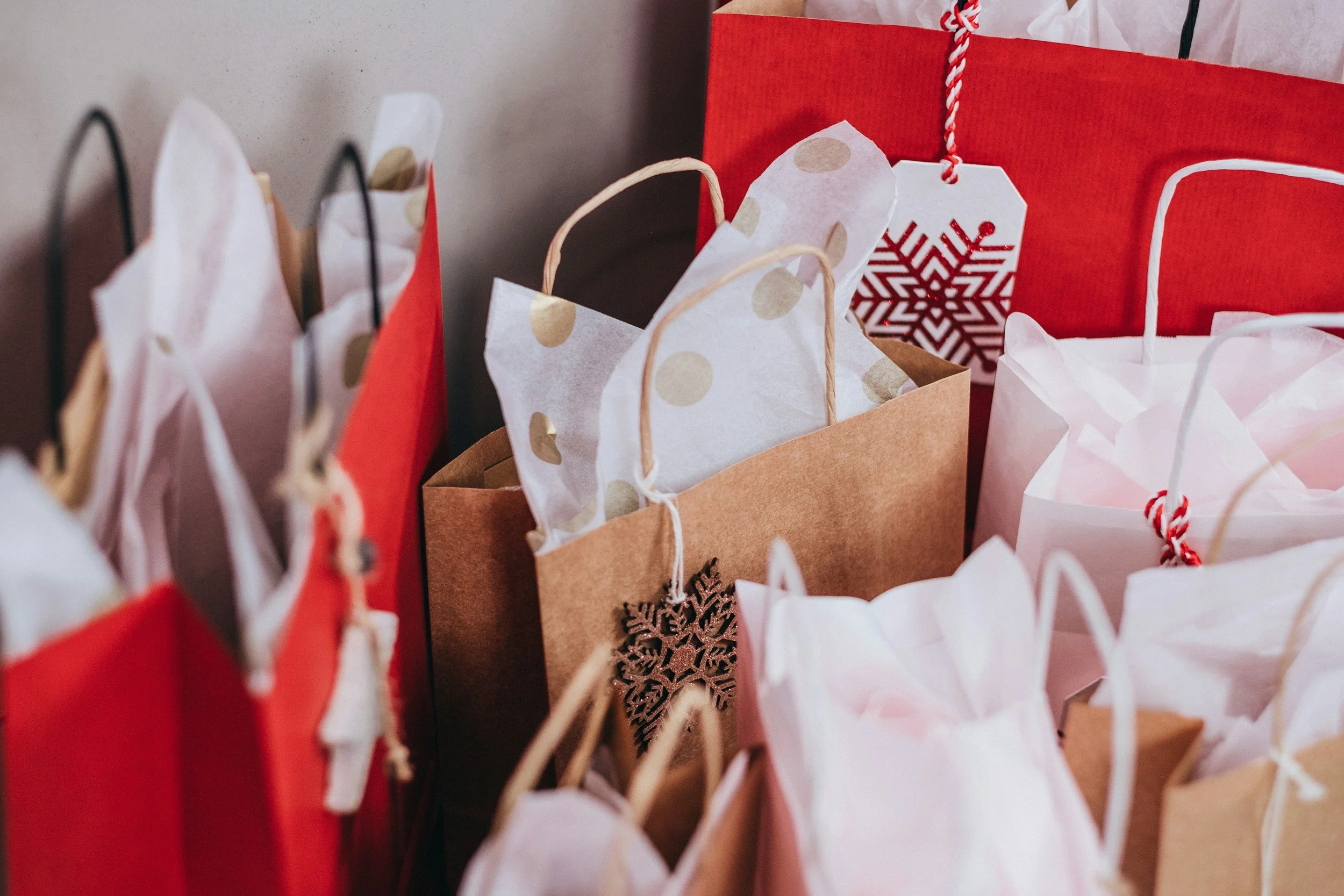 Multiple Christmas gift bags in red, white, pink, and brown with tissue paper and decorative snowflake ornaments.