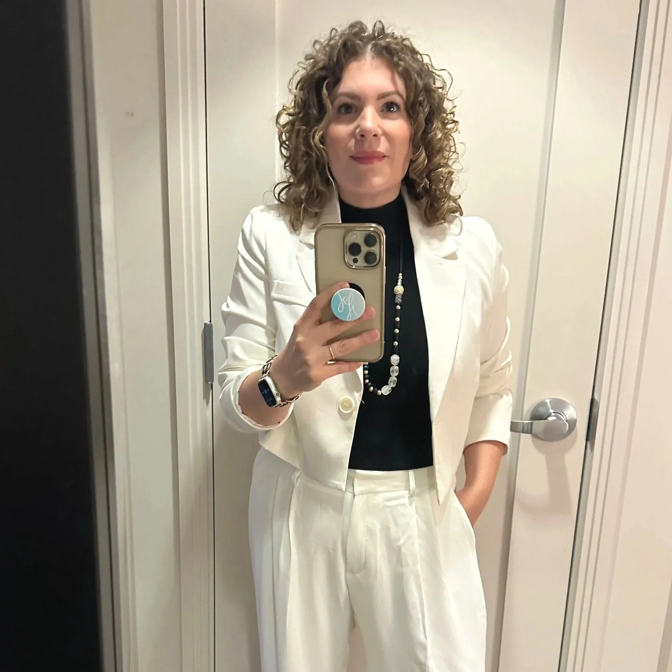 Selfie of one of Jenna's clients wearing a white suit with a black top and beaded necklace