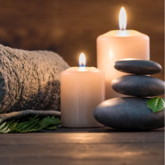 two lit white candles behind a stack of three dark grey stones