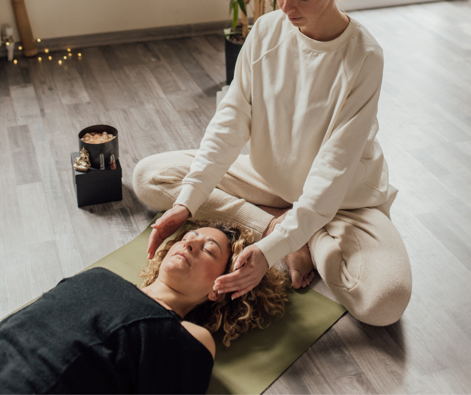 a woman lying on a yoga mat with a Reiki practitioner's hands a few inches away from each side of her head