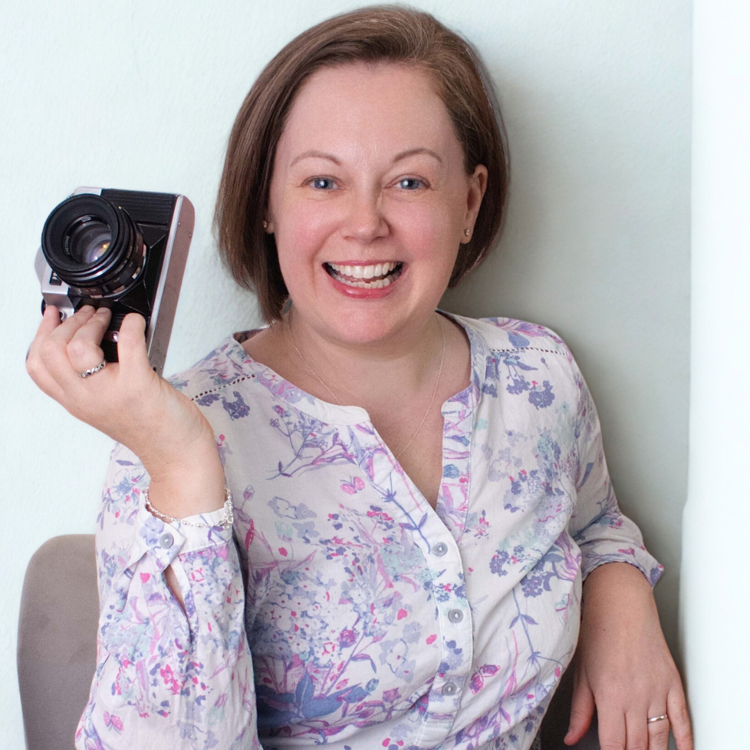 A woman wearing a bright orange vest poses on the beach in pigeon pose. 
