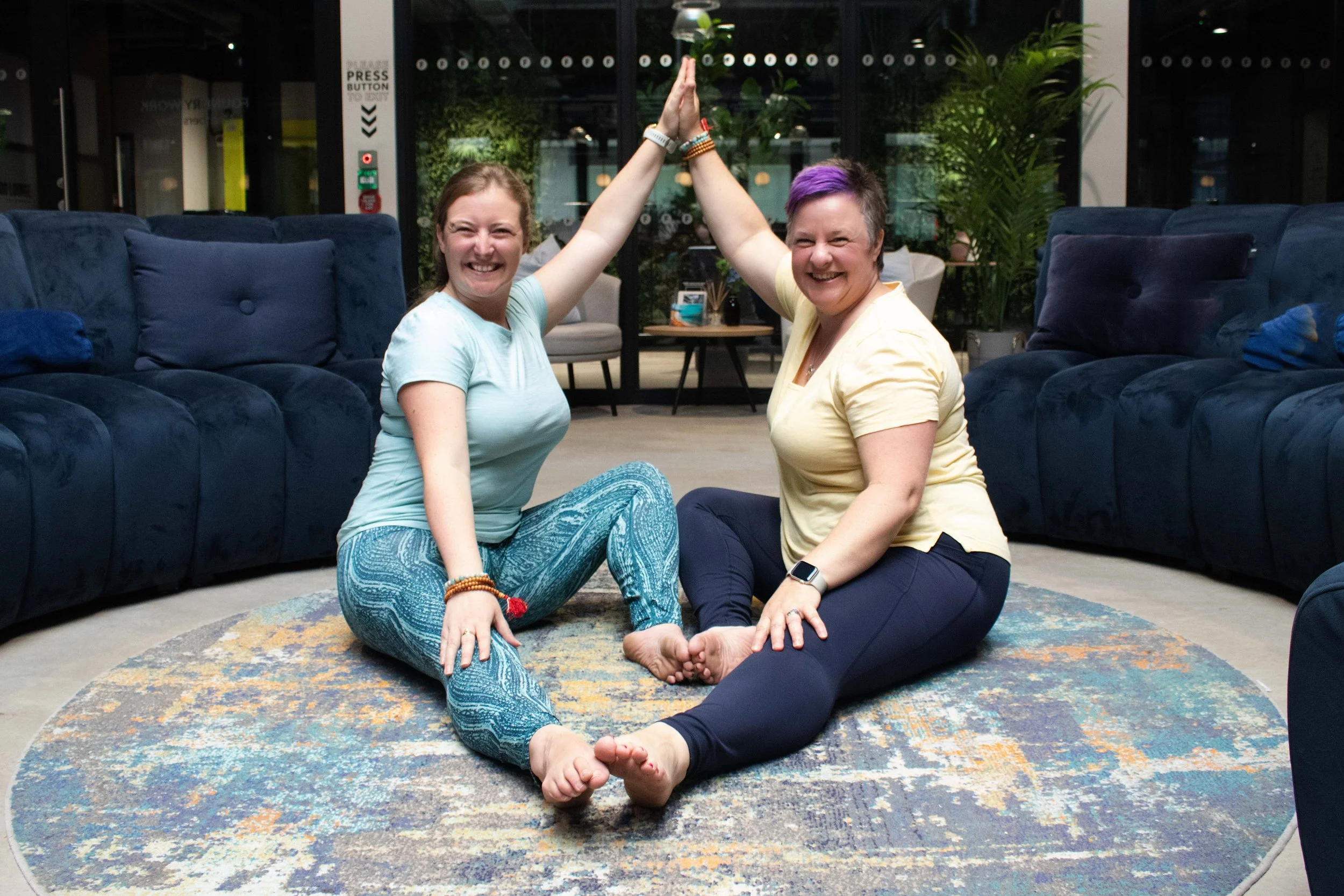 two women sit in a yoga pose with their hands touching forming. asymmetrical shape