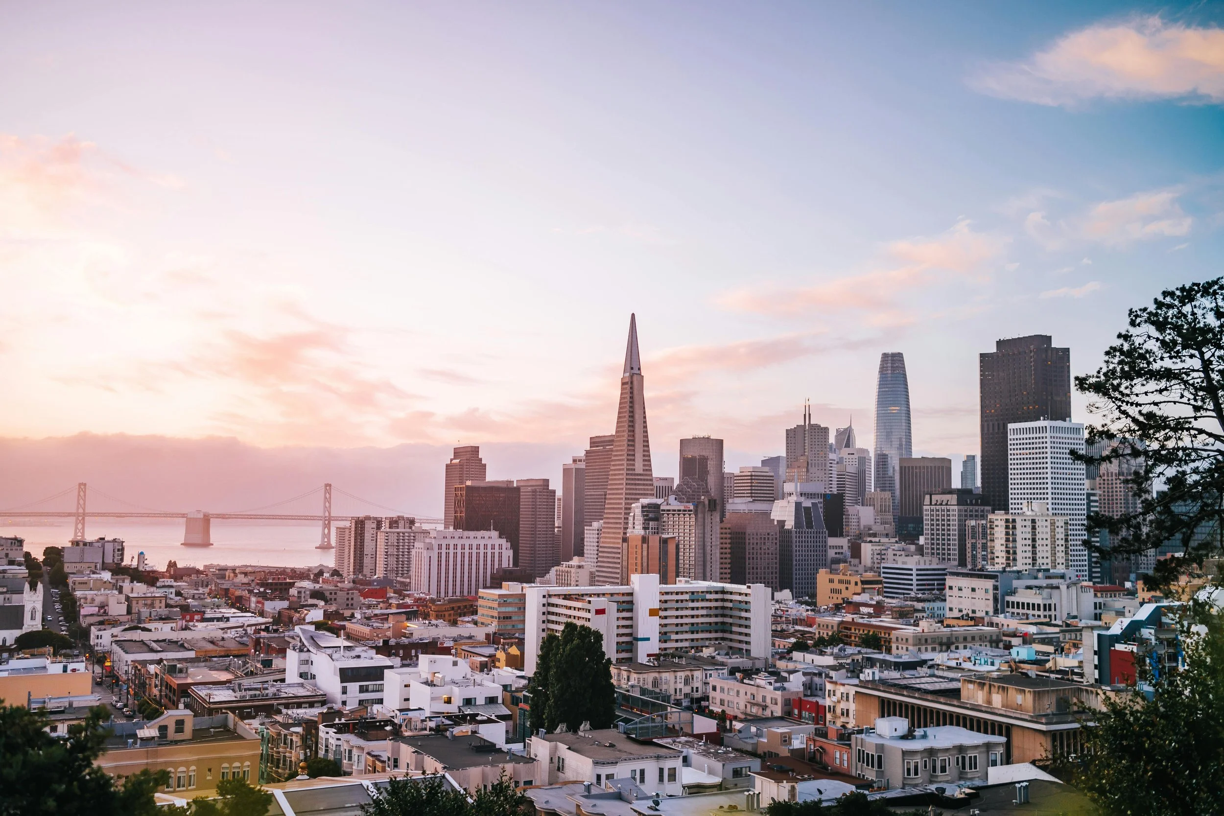 Sunset over downtown San Francisco with city skyline including Salesforce Tower and the Bay Bridge.