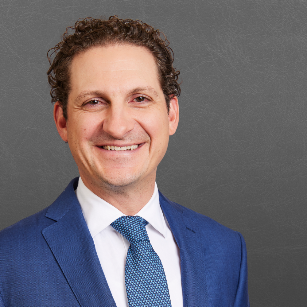 Portrait of a smiling man in a blue suit and tie against a gray background.