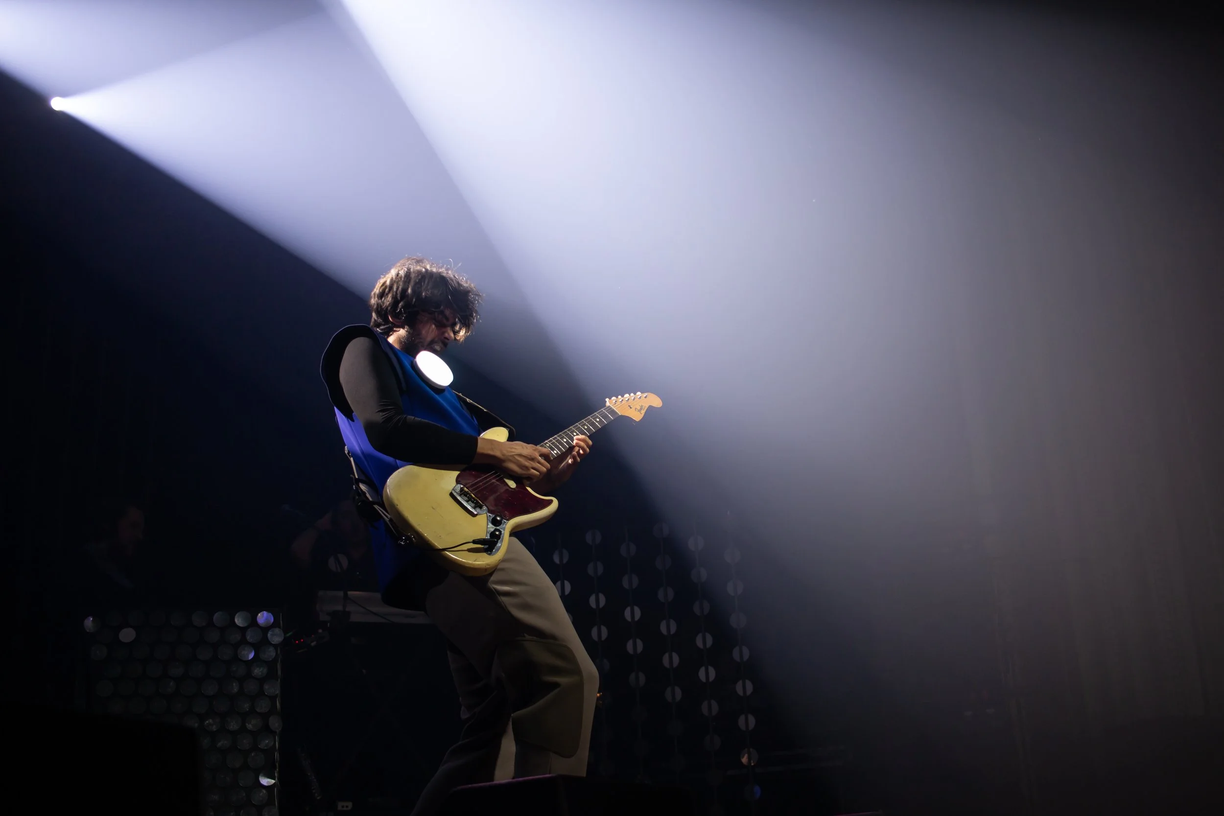 Musicien jouant de la guitare électrique sur scène avec un éclairage dramatique.