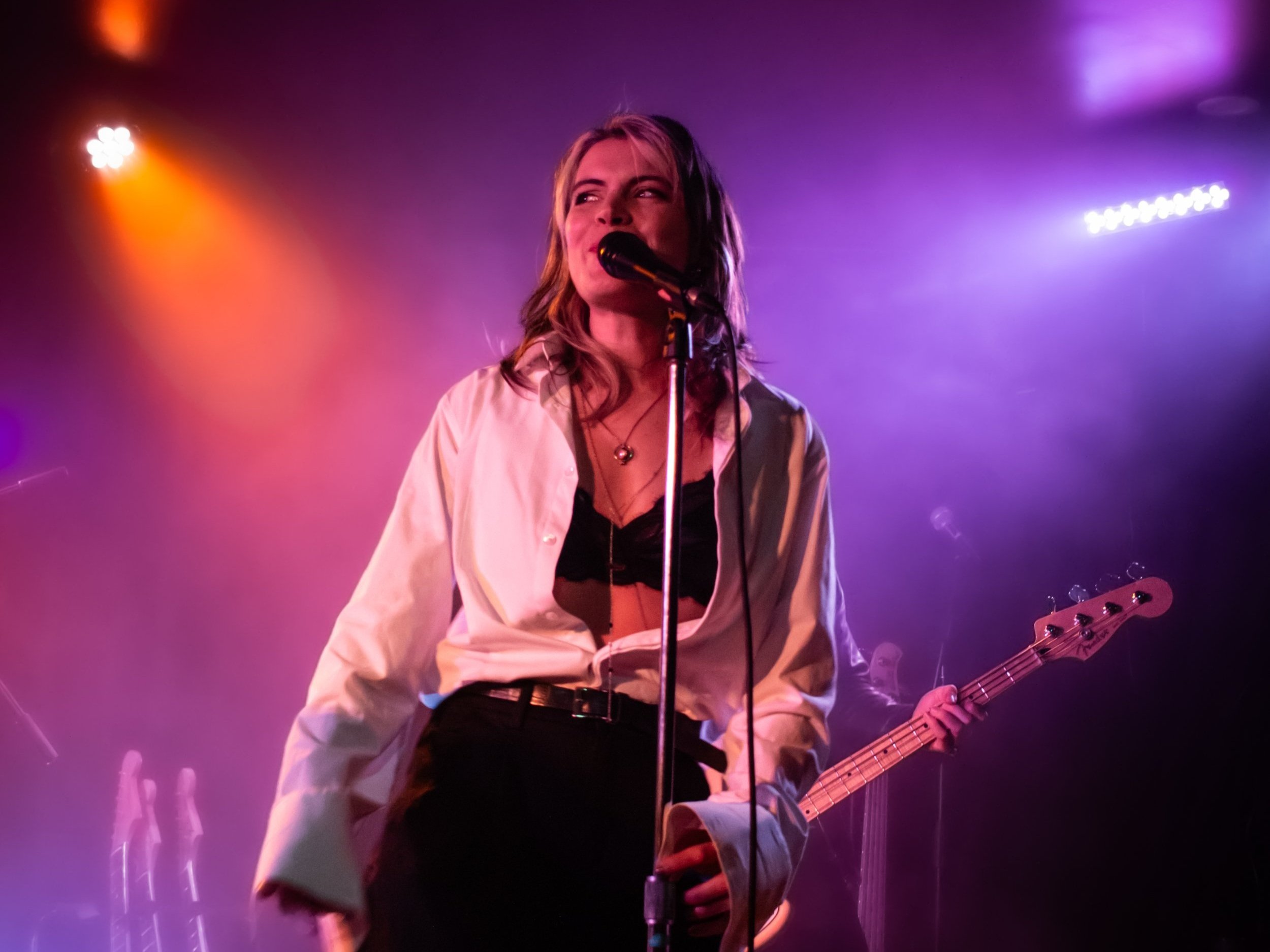 Une femme chante avec un micro lors d'une performance musicale, entourée d'éclairage coloré violet et orange sur scène.