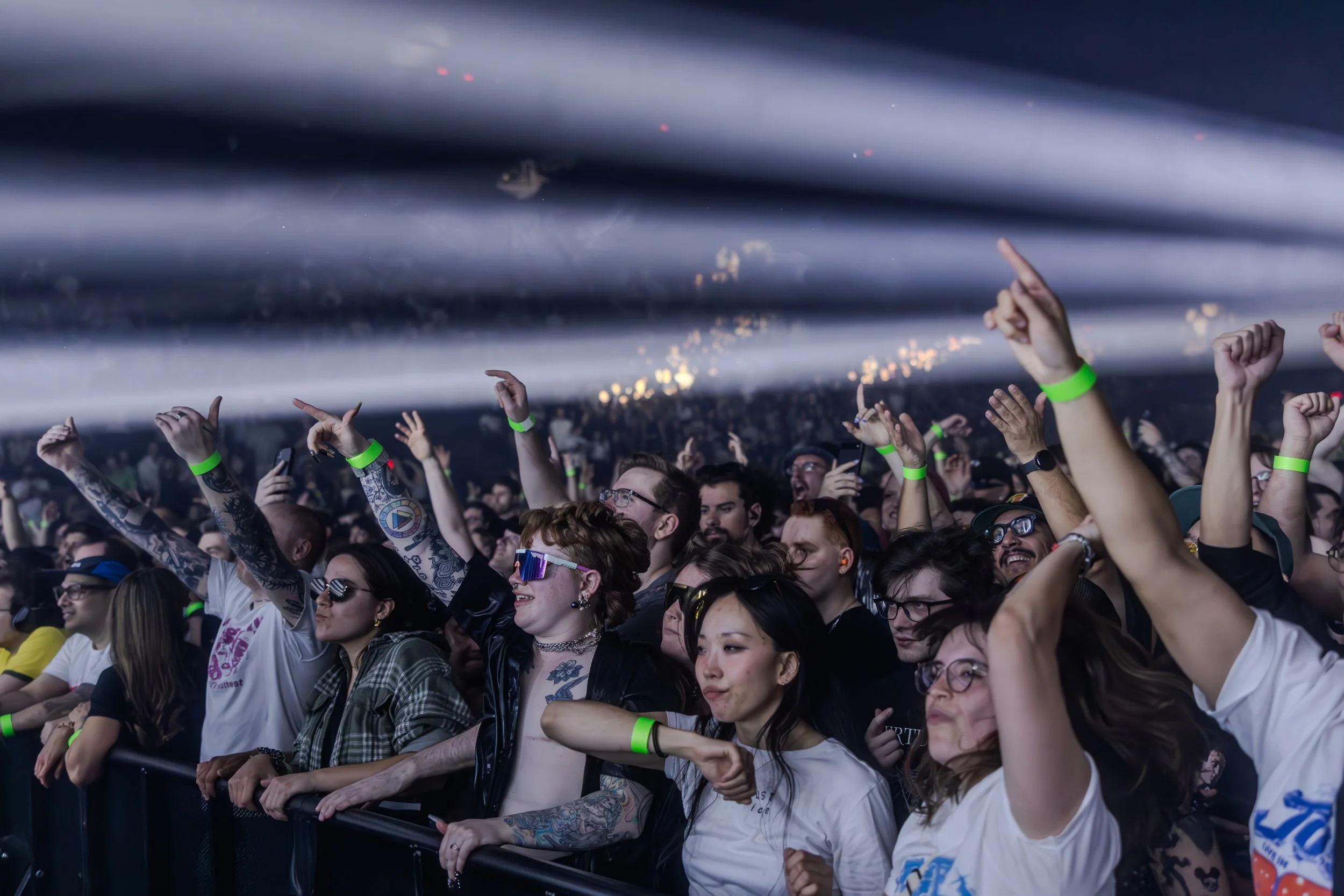 Une foule de personnes à un concert, many portant des bracelets lumineux verts, dans une ambiance festive avec des lumières et une scène en arrière-plan.