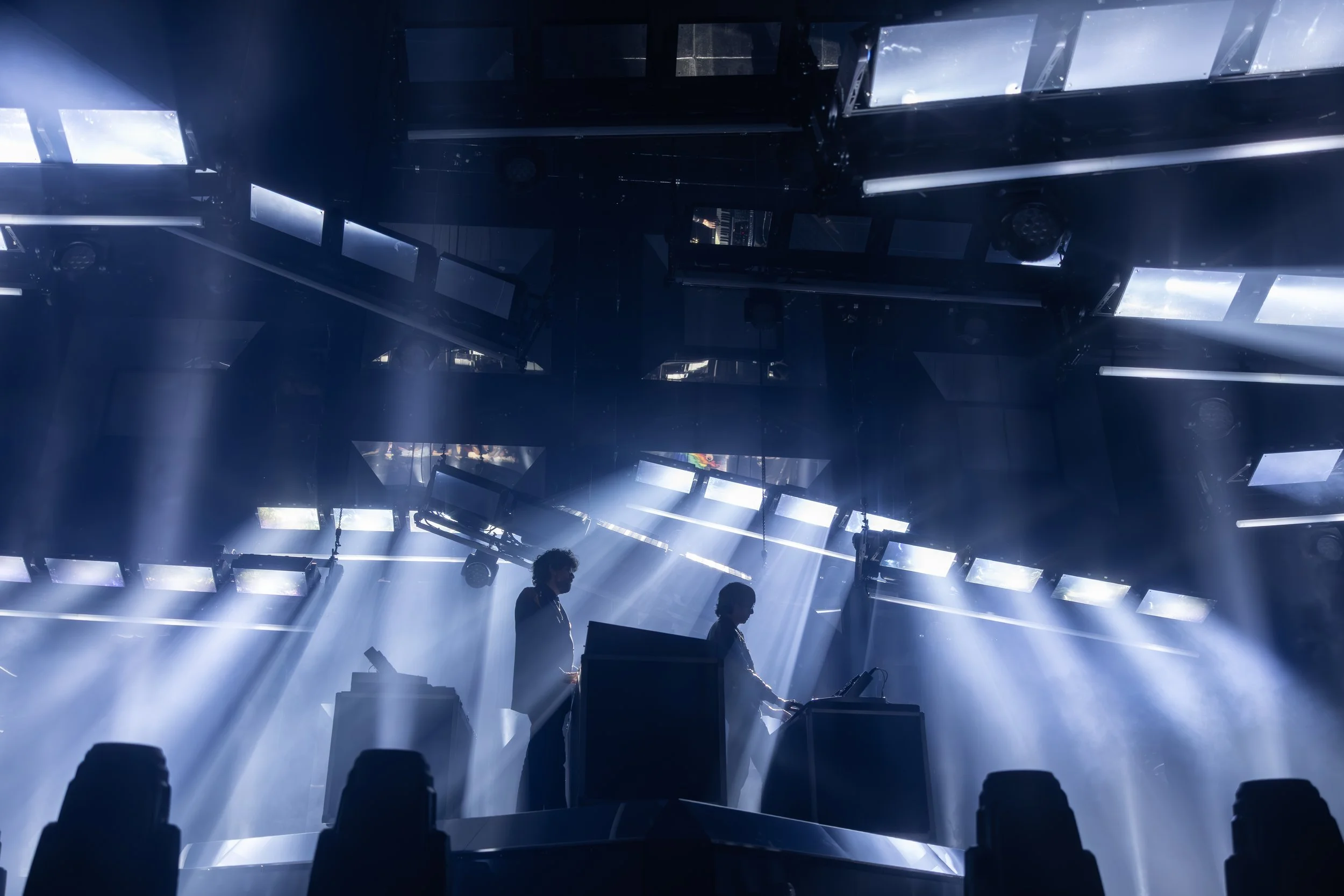 Scène de concert avec deux DJ sur scène, éclairage intense et rayons lumineux créant une atmosphère dynamique