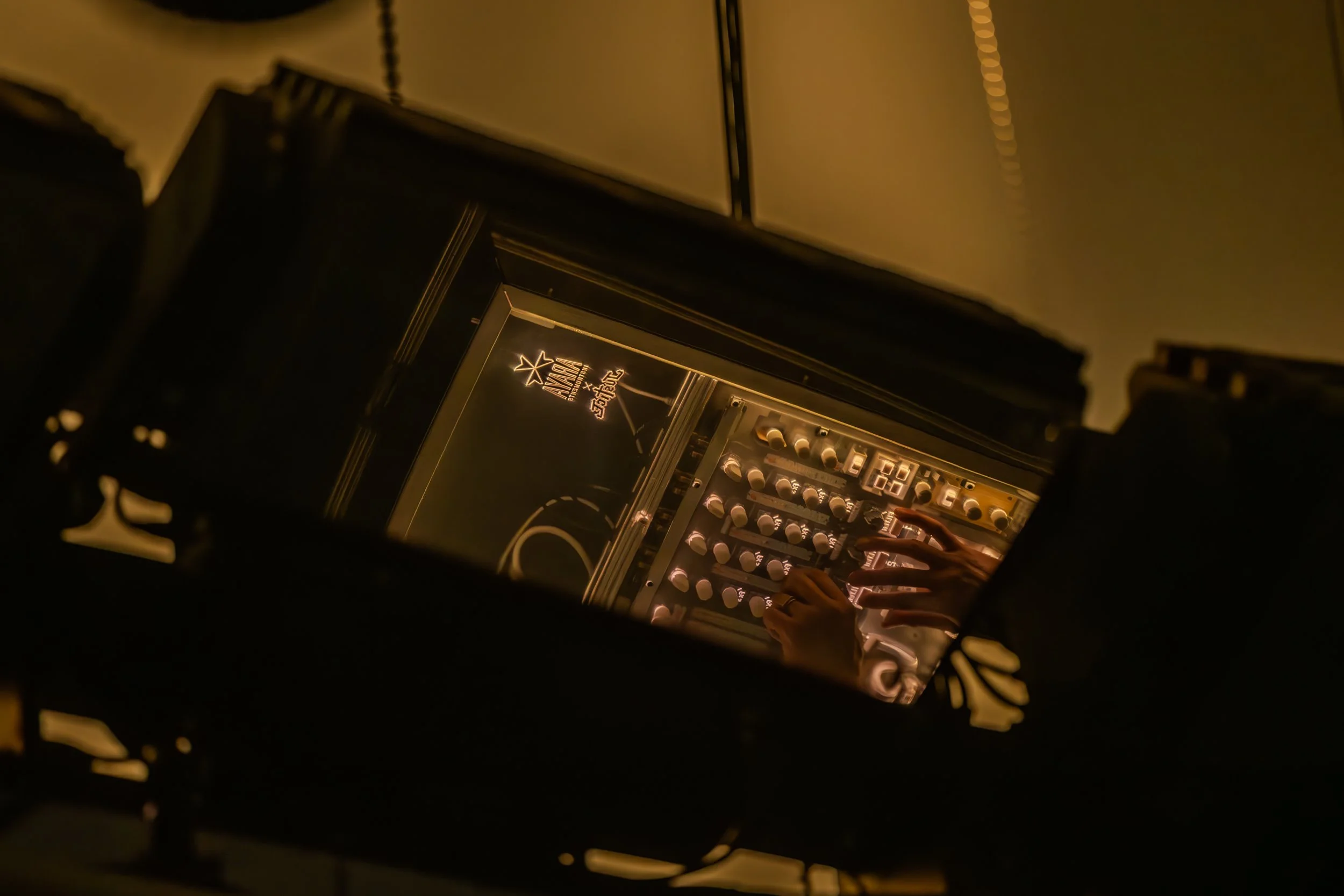 Reflet d'une main manipulant des boutons d'un clavier de synthétiseur ou d'un dispositif de musique électronique, avec une marque ou un logo visible sur un panneau lumineux, dans un environnement sombre.