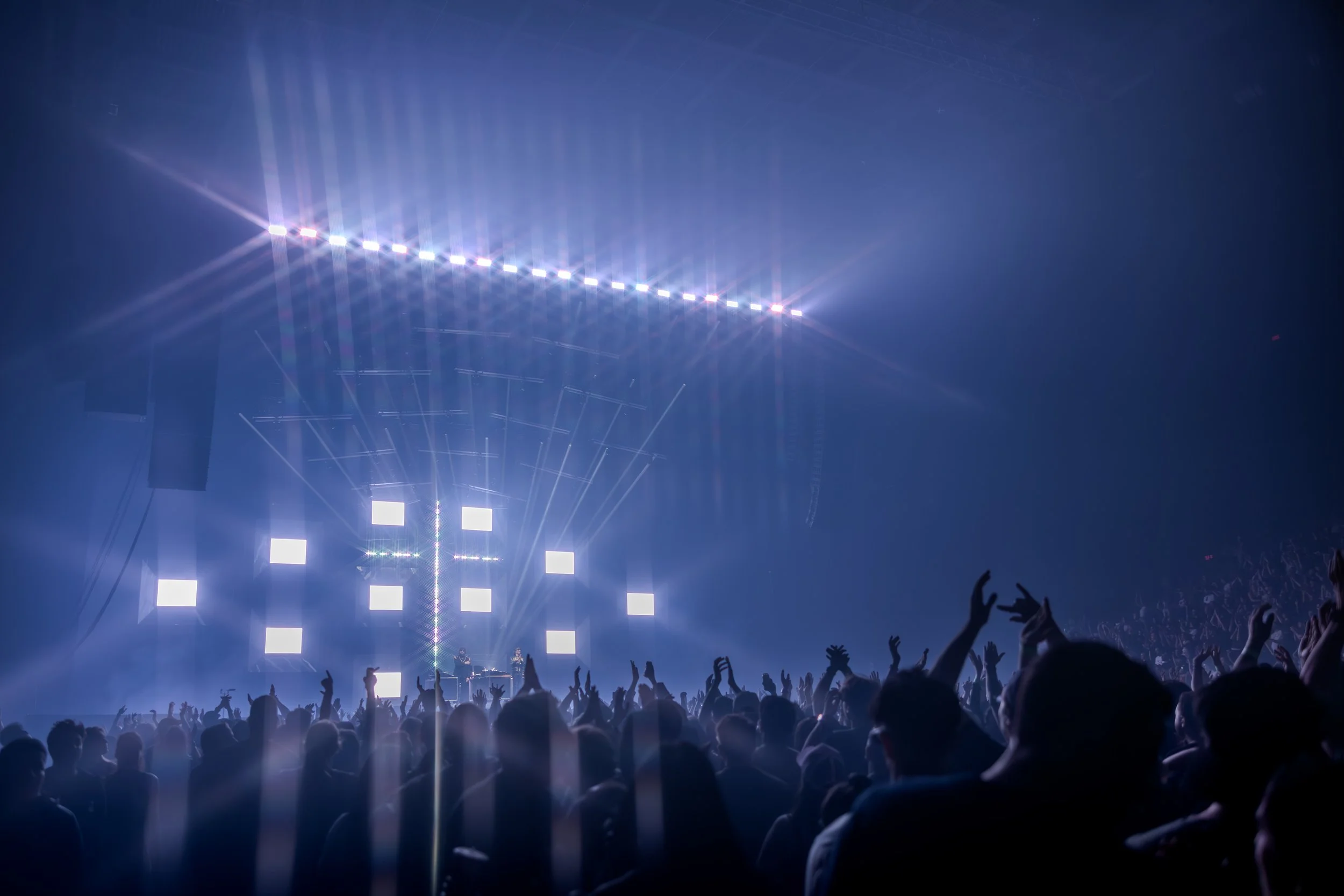 Une scène de concert avec un public nombreux, des lumières vives et une scène avec des écrans lumineux.